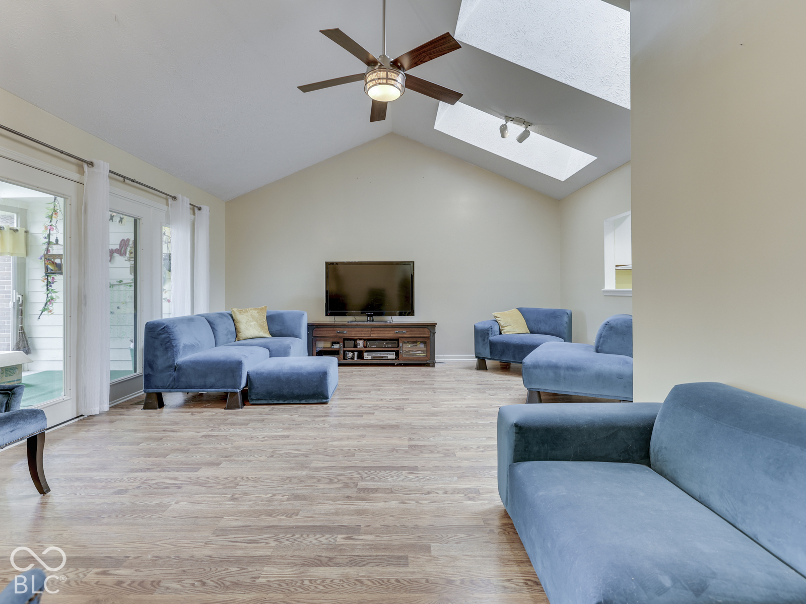 Vaulted ceiling featuring skylights, wood-finish flooring, and a ceiling fan with integrated lighting