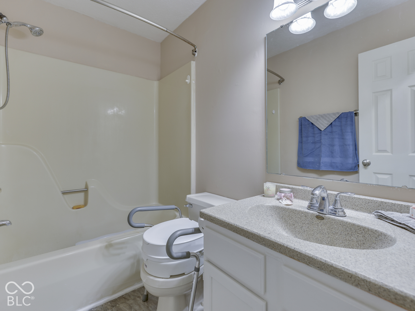 Bathroom featuring a vanity with a solid-surface integrated sink, molded tub surround, polished chrome faucet hardware, and a large-format vanity mirror with integrated multi-bulb lighting