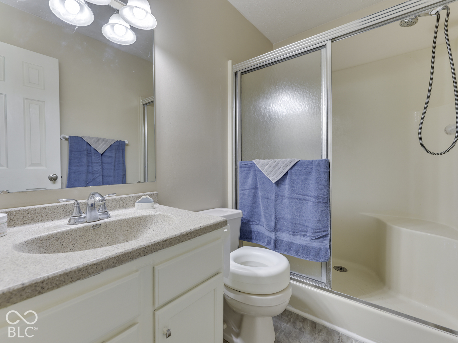 Bathroom featuring a vanity with an integrated countertop and sink, framed mirror with integrated vanity lighting, and a shower enclosure with sliding glass doors and a built-in seat
