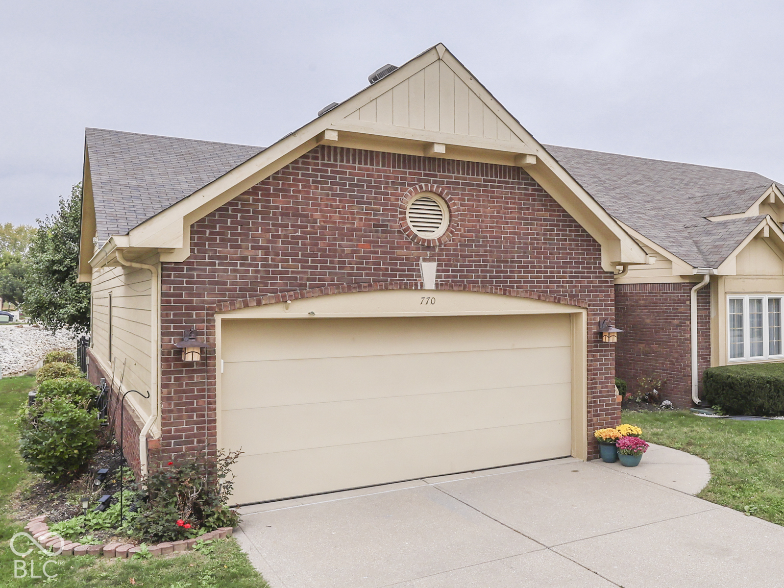 Brick exterior with horizontal siding gables, asphalt shingle roofing, attached two-car garage with arched header, and decorative circular gable vent