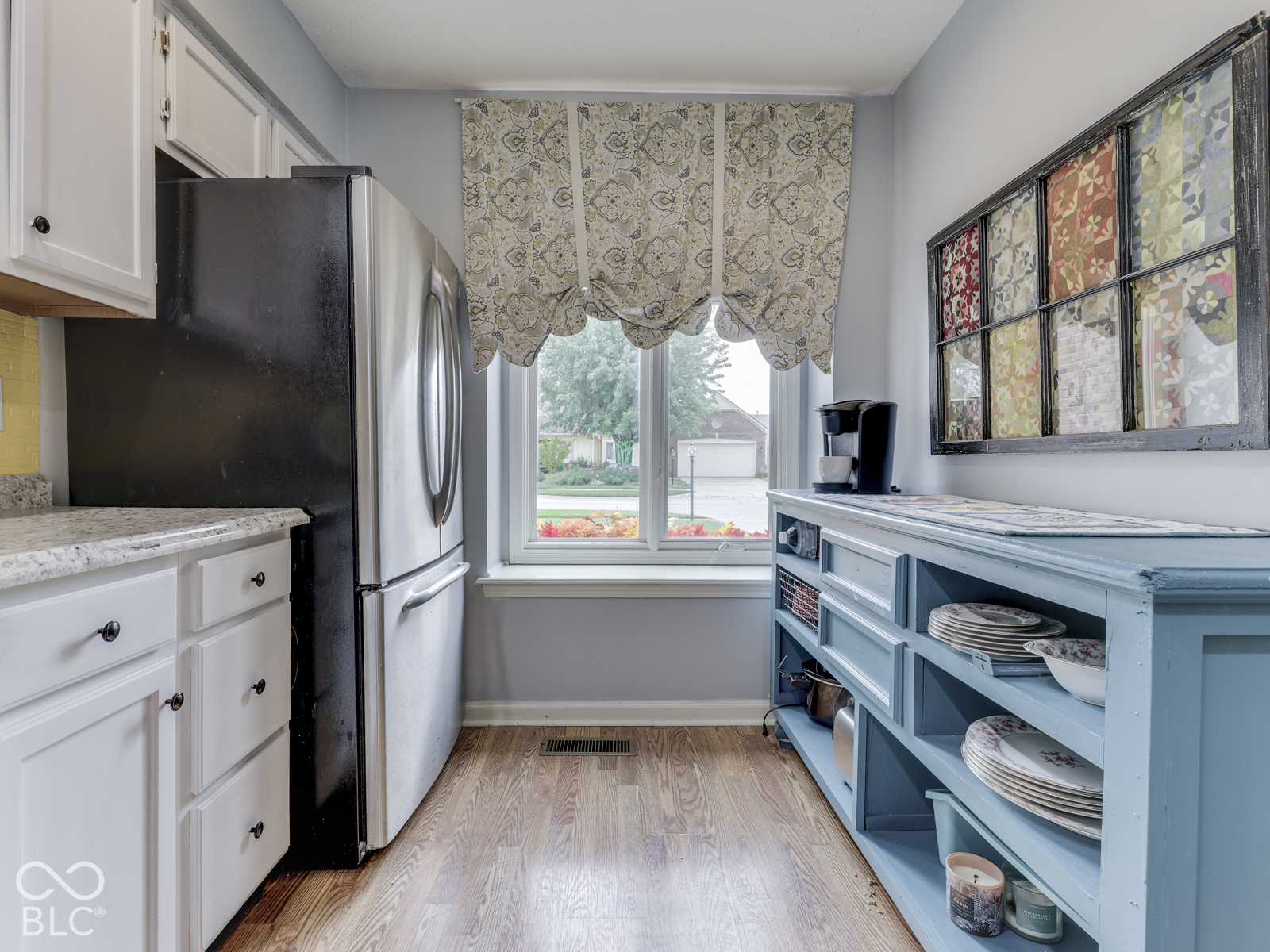 Kitchen featuring white cabinetry, wood-finish flooring, stainless steel refrigerator, and a window centered above the floor space