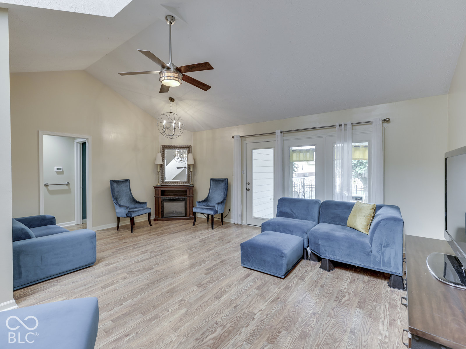 Vaulted ceilings, wood-finish flooring, built-in corner fireplace, ceiling fan with light fixture, and glass-paneled exterior door