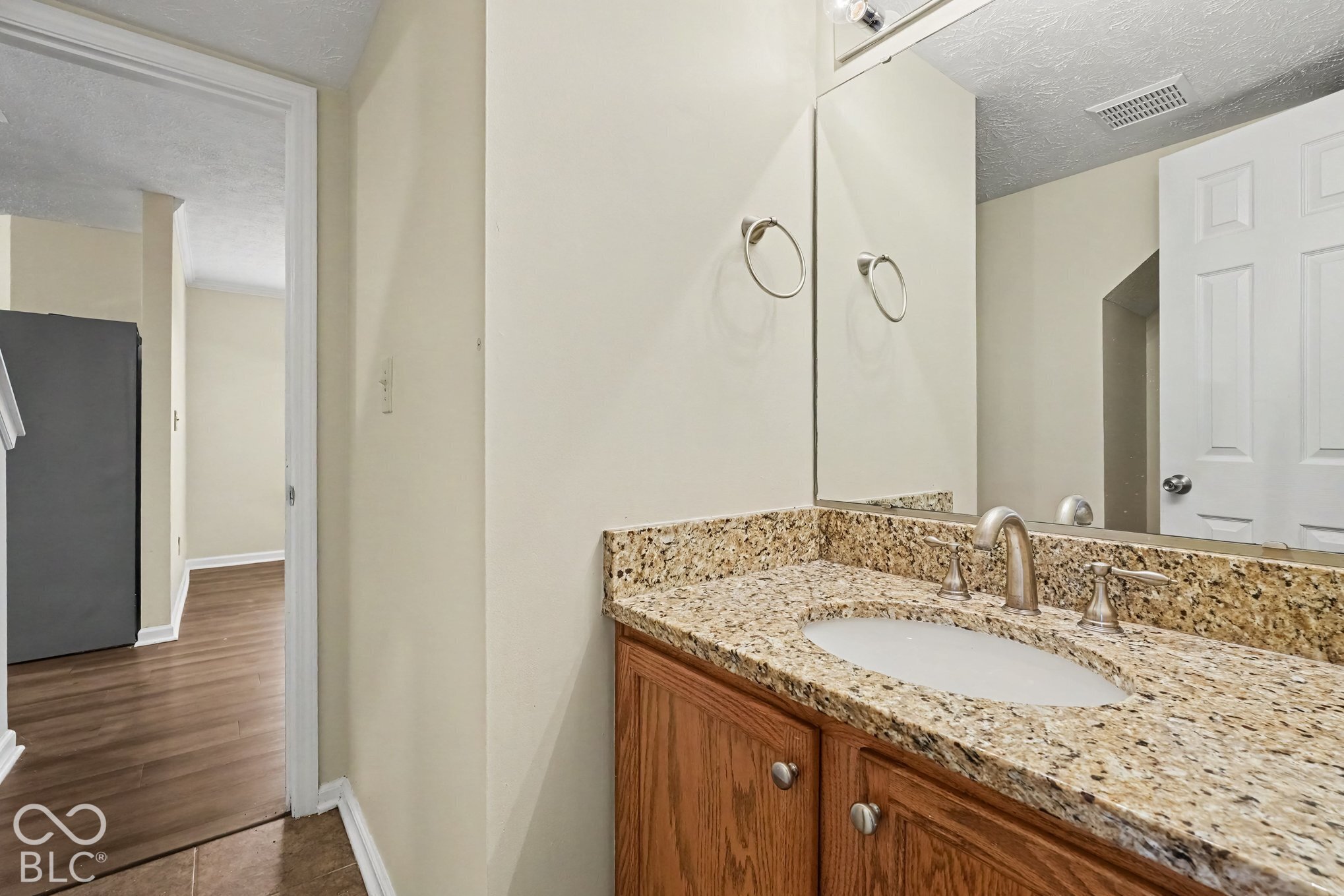 Vanity featuring a stone-finish countertop, undermount sink, dual-handle faucet, and wooden cabinetry, paired with a wall-mounted mirror