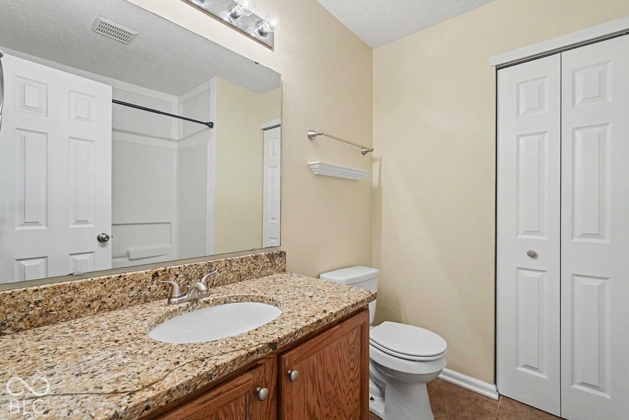 Bathroom featuring a stone-pattern vanity countertop with an integrated oval basin, wooden cabinetry, a full-width wall mirror, and bi-fold closet doors