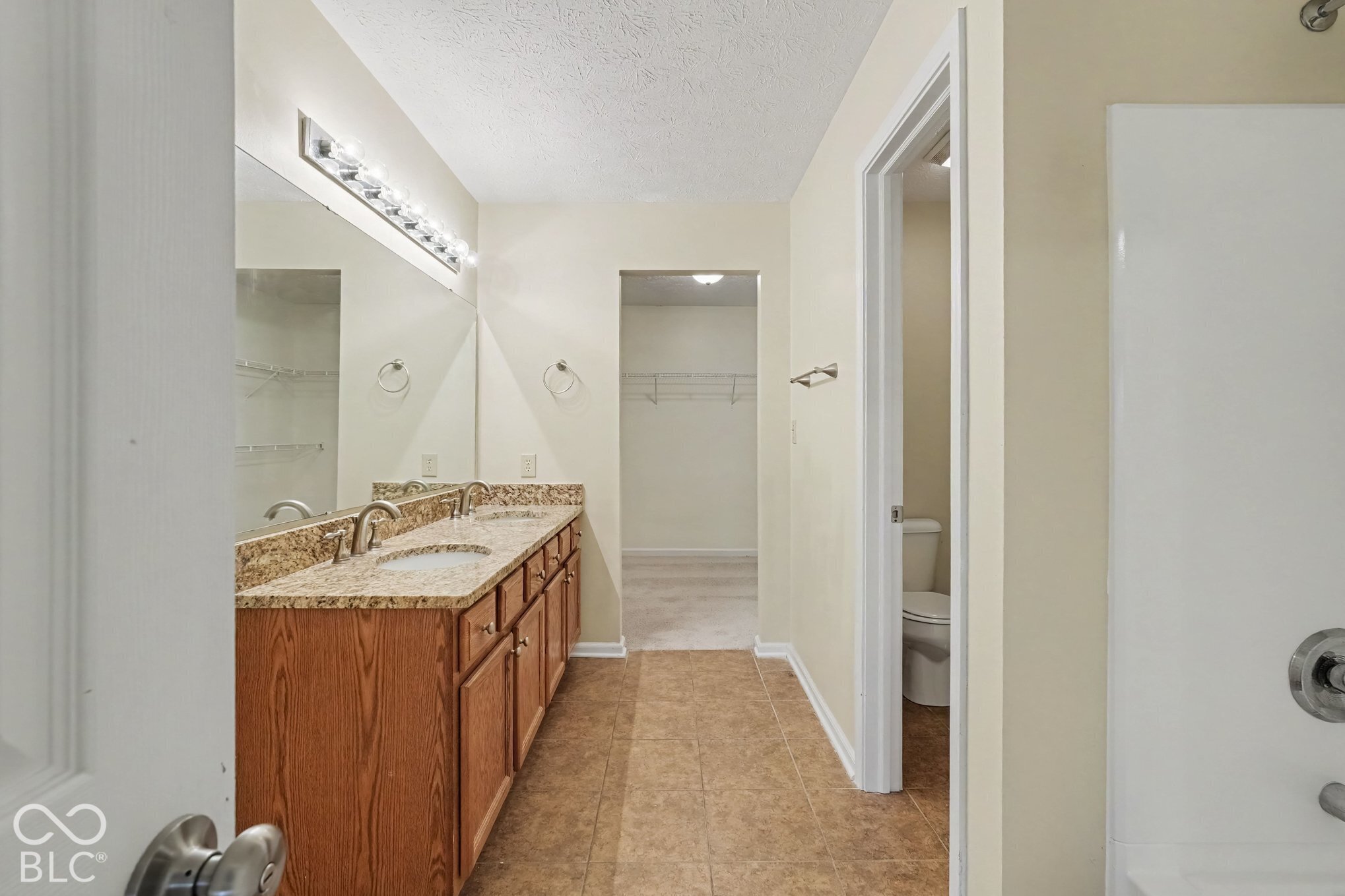 Bathroom featuring a double vanity with stone-finish countertop, dual under-mount sinks, wood-finish cabinetry, and a full-width wall mirror