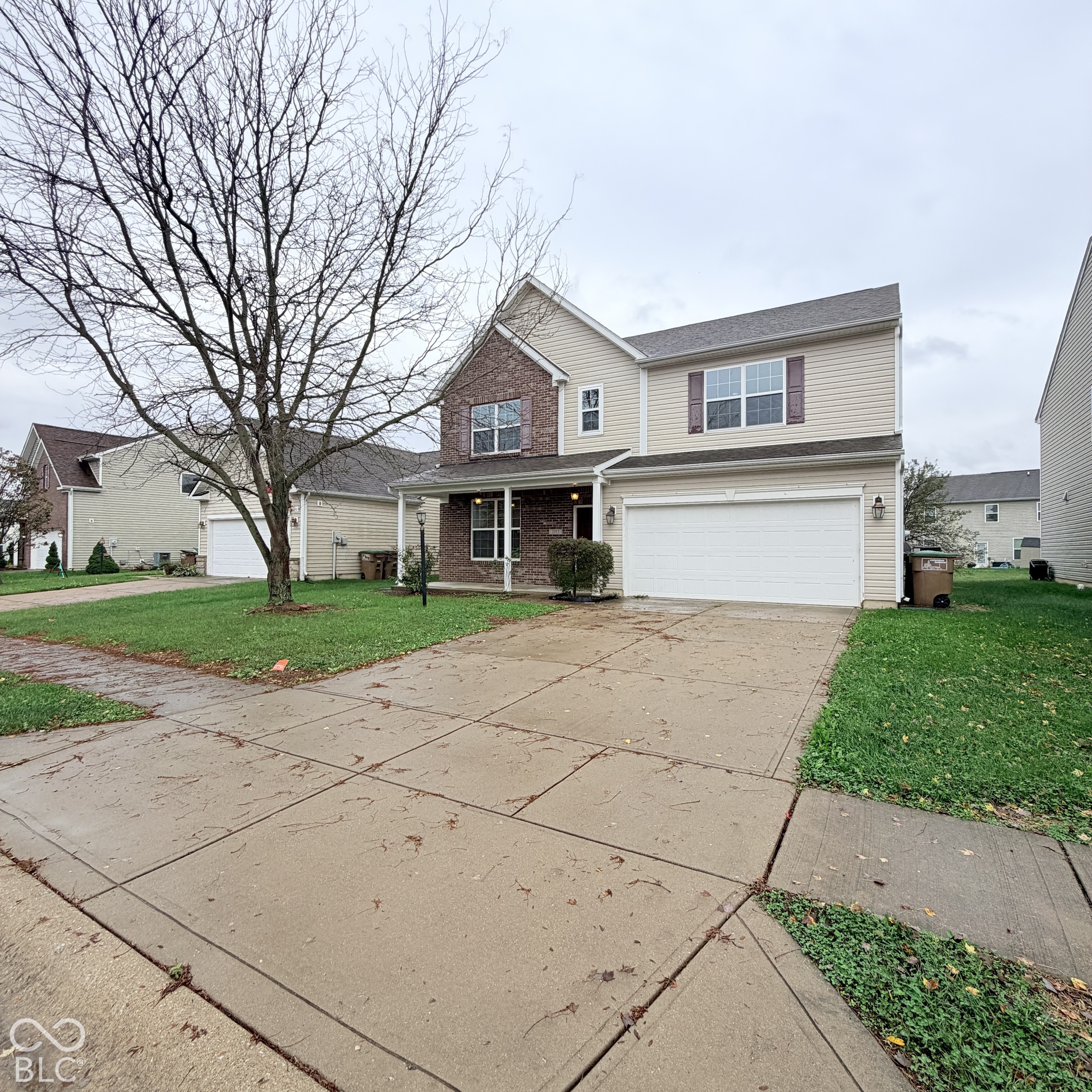 Two-story residence featuring light-colored vinyl siding, partial brick facade, attached two-car garage, and a concrete driveway Two-story residence featuring light-colored vinyl siding, partial brick facade, attached two-car garage, and a concrete driveway