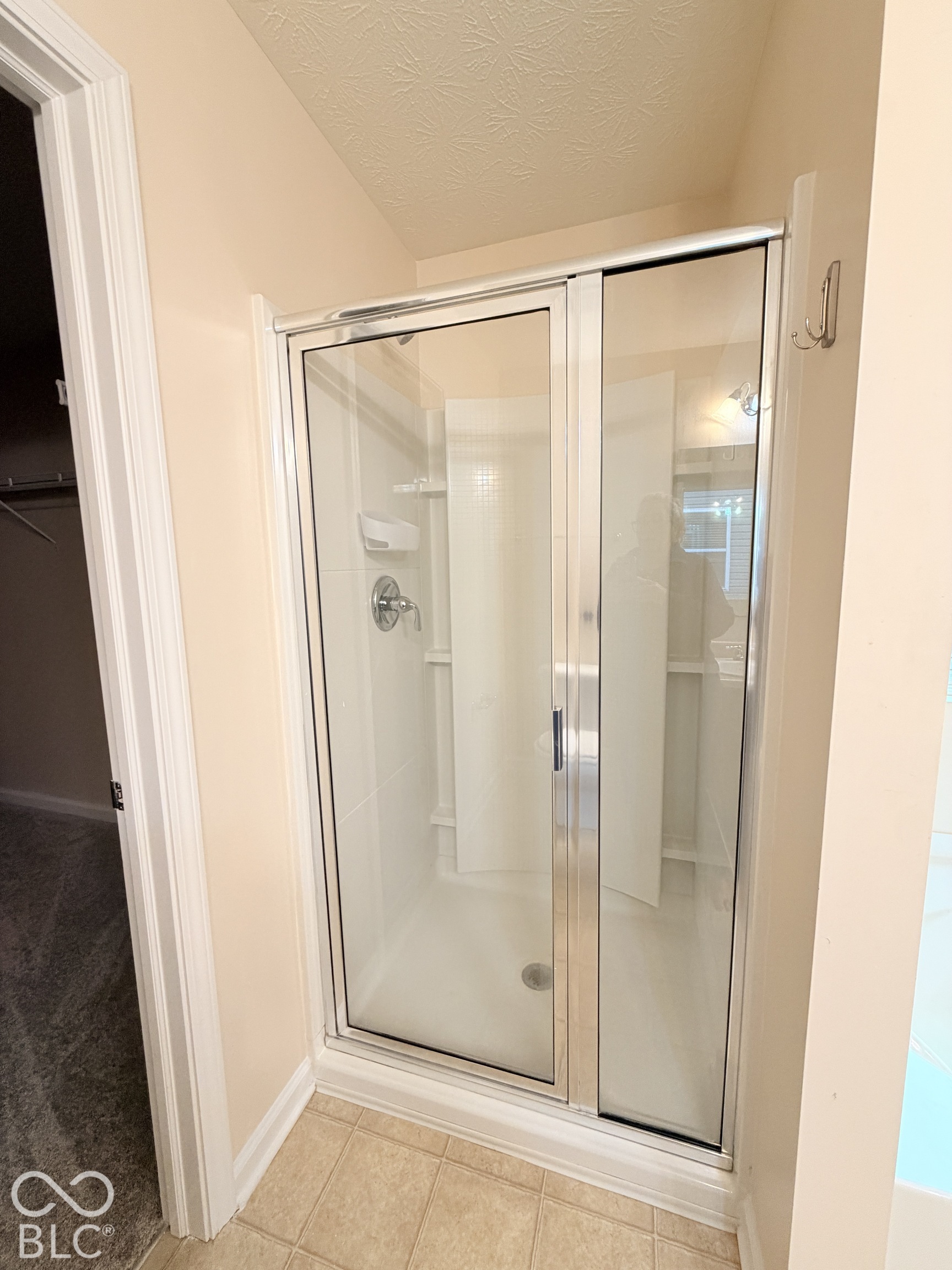 Shower enclosure featuring a chrome-framed glass door, integrated wall surround, built-in shelving, and a chrome single-handle faucet
