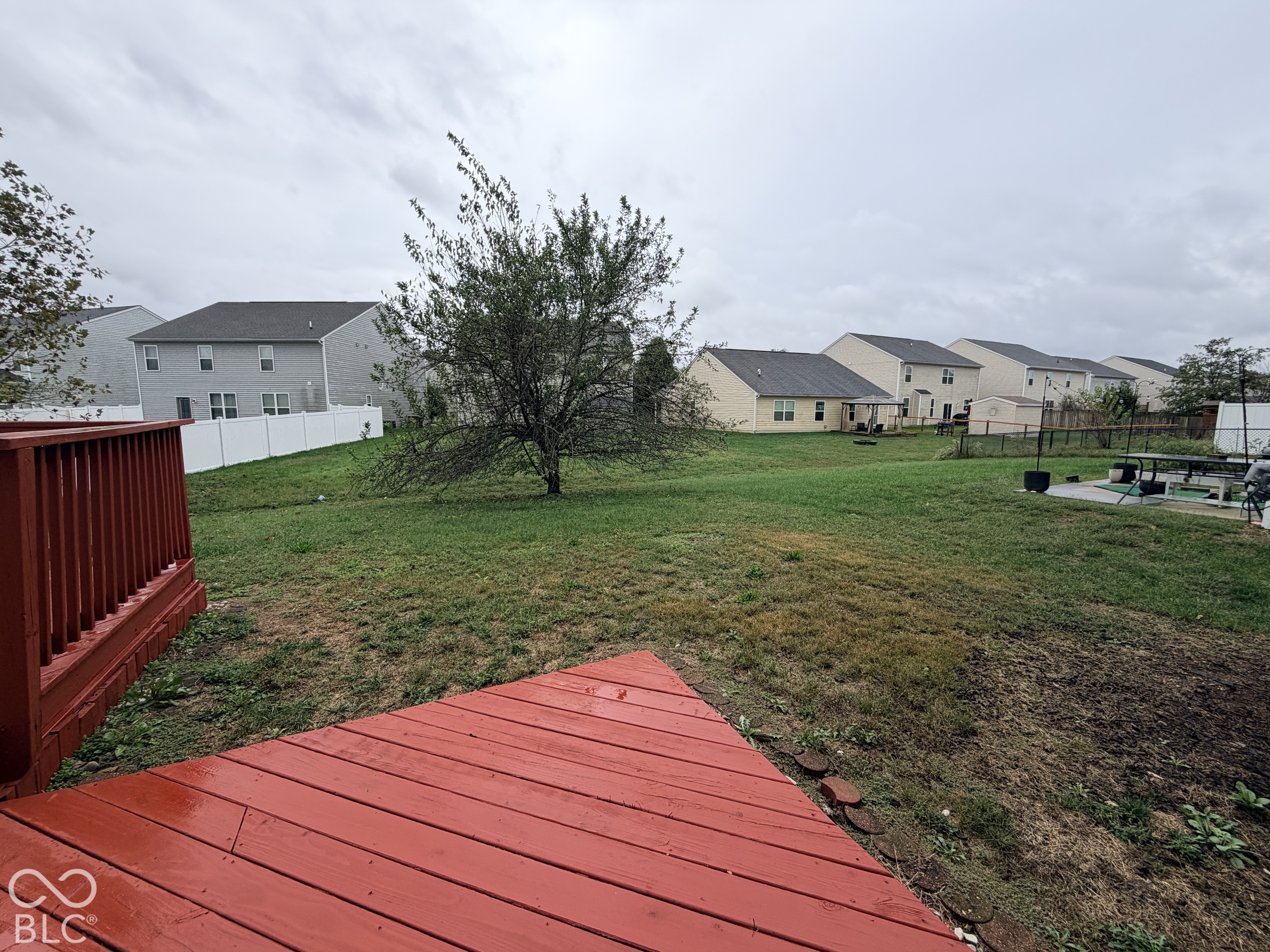 Rear wooden deck featuring a painted finish and railing, opening to a grass yard with a perimeter white vinyl privacy fence
