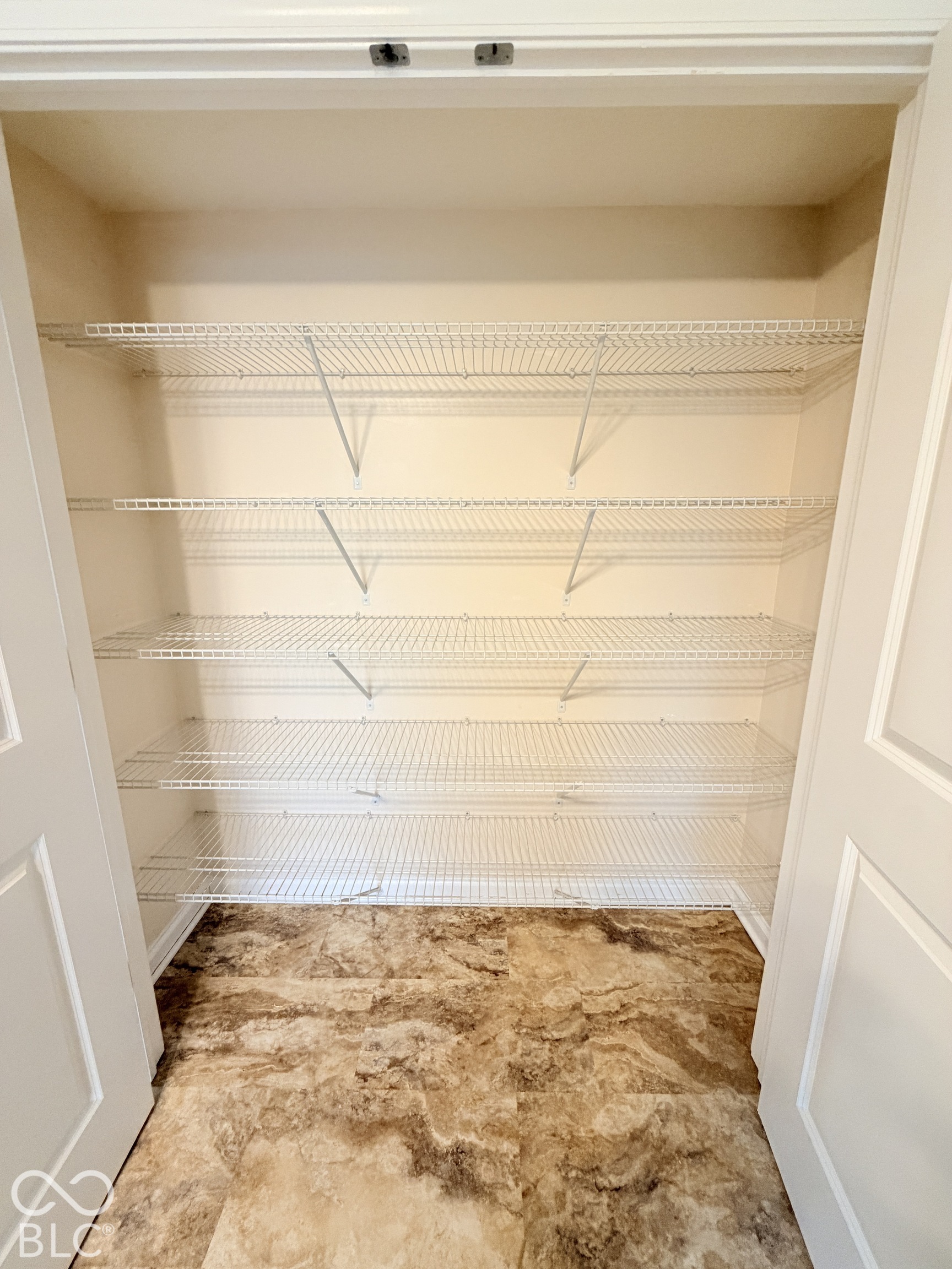 Storage area featuring five tiers of white wire shelving and patterned floor tiling