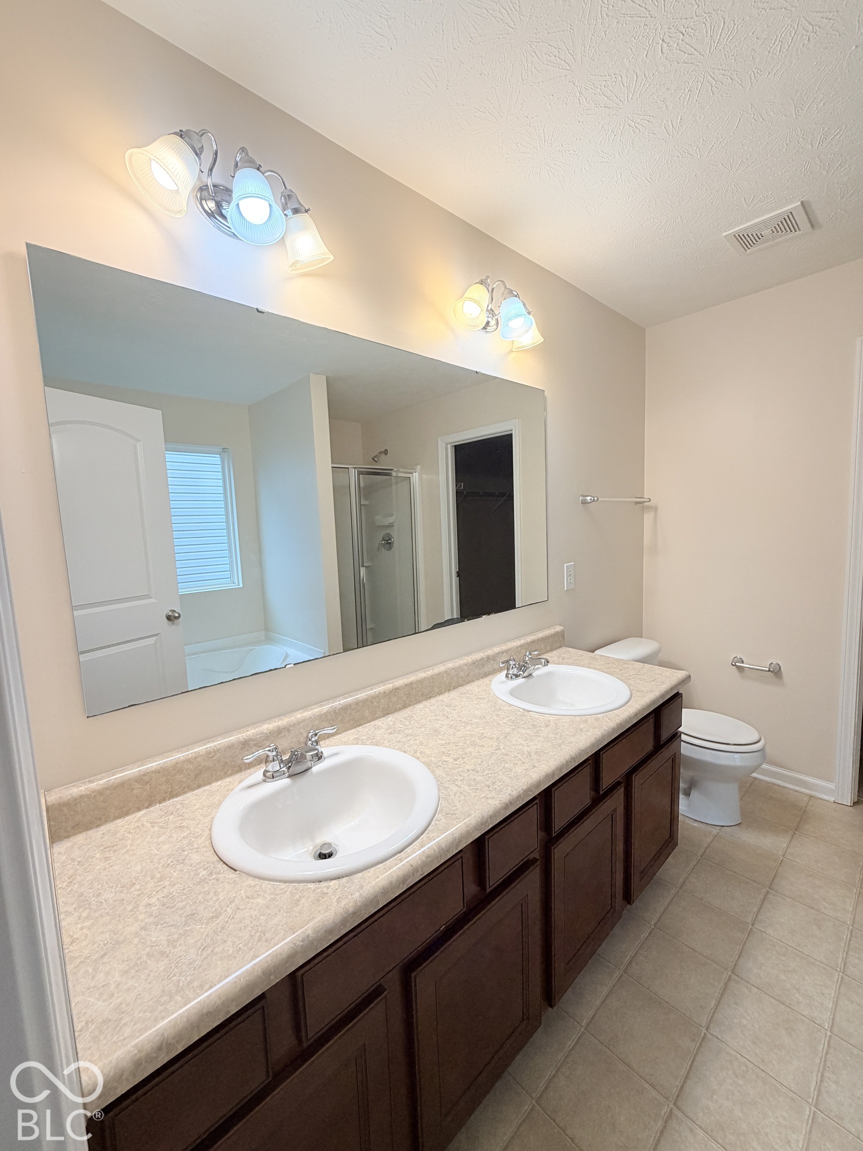 Dual-sink vanity with stone-finish countertop, dark wood-finish cabinetry, full-width wall mirror, and dual multi-light fixtures