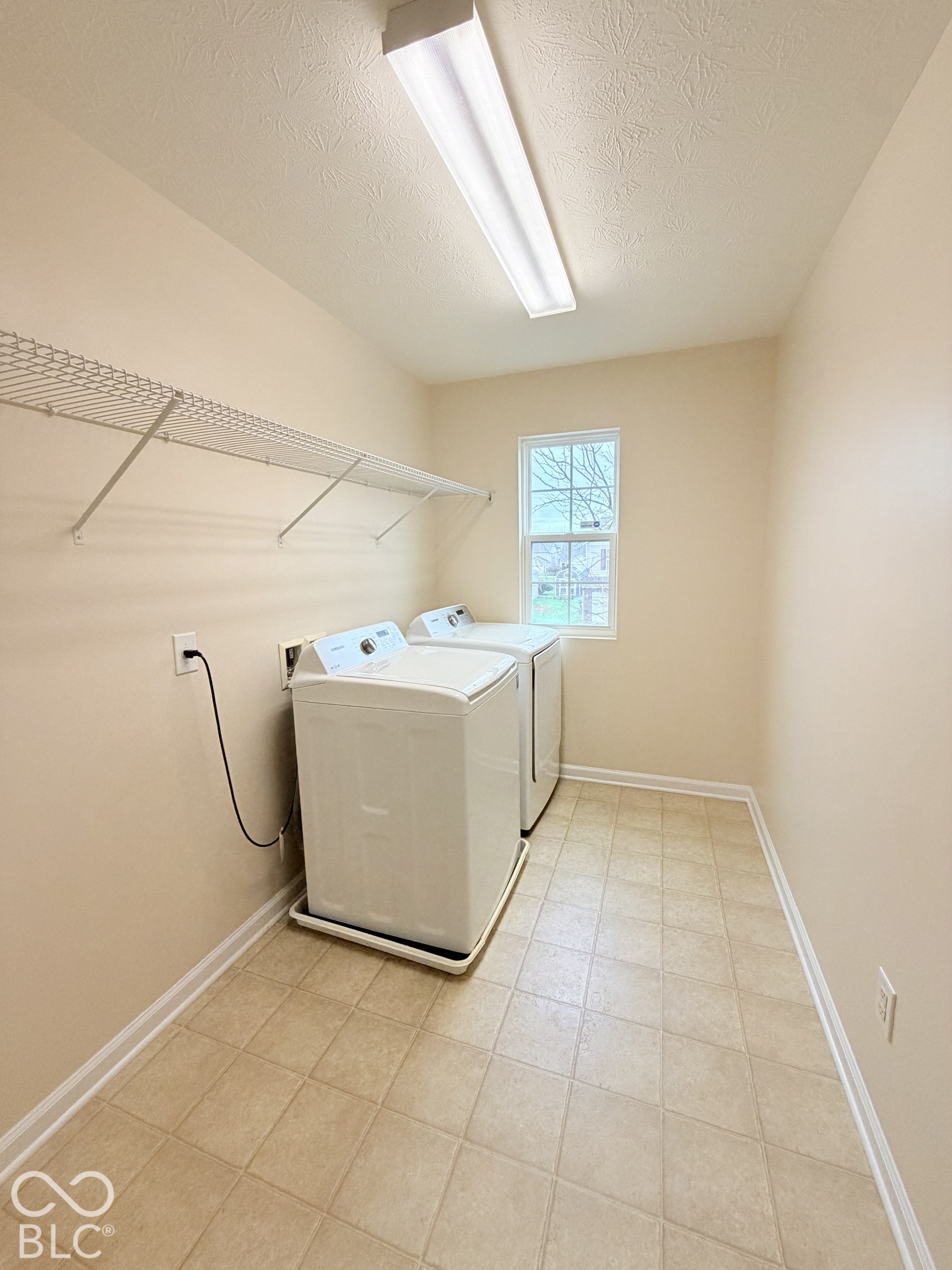 Utility space featuring neutral walls, tile-patterned flooring, a single-hung window, and wall-mounted wire shelving