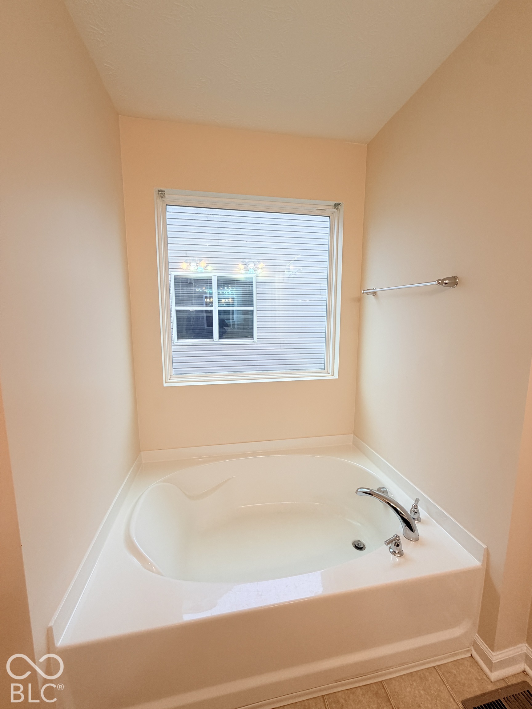Soaking tub featuring a tiled deck, brushed-nickel faucet, and a wall-mounted towel bar