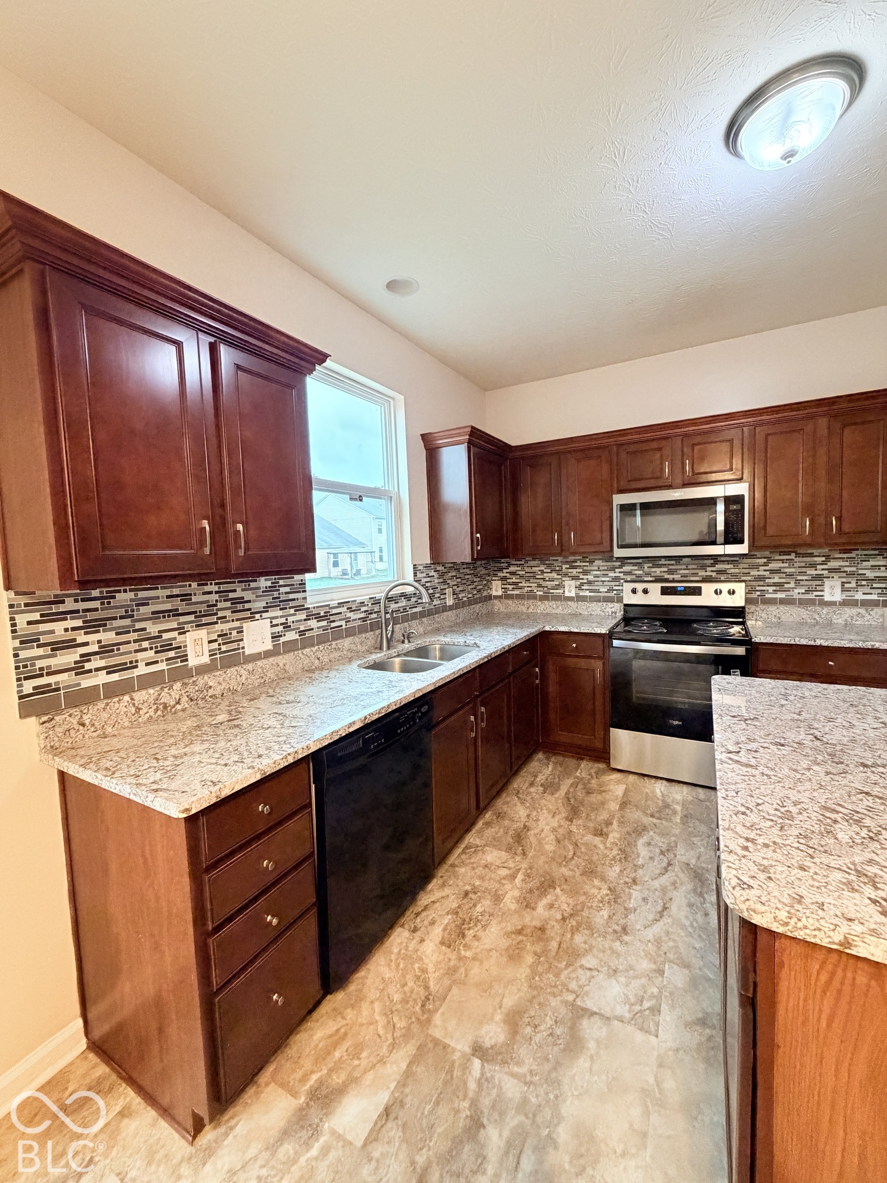 Kitchen featuring stained wood cabinetry, stone-patterned countertops, a decorative mosaic tile backsplash, stainless steel appliances, and tile flooring