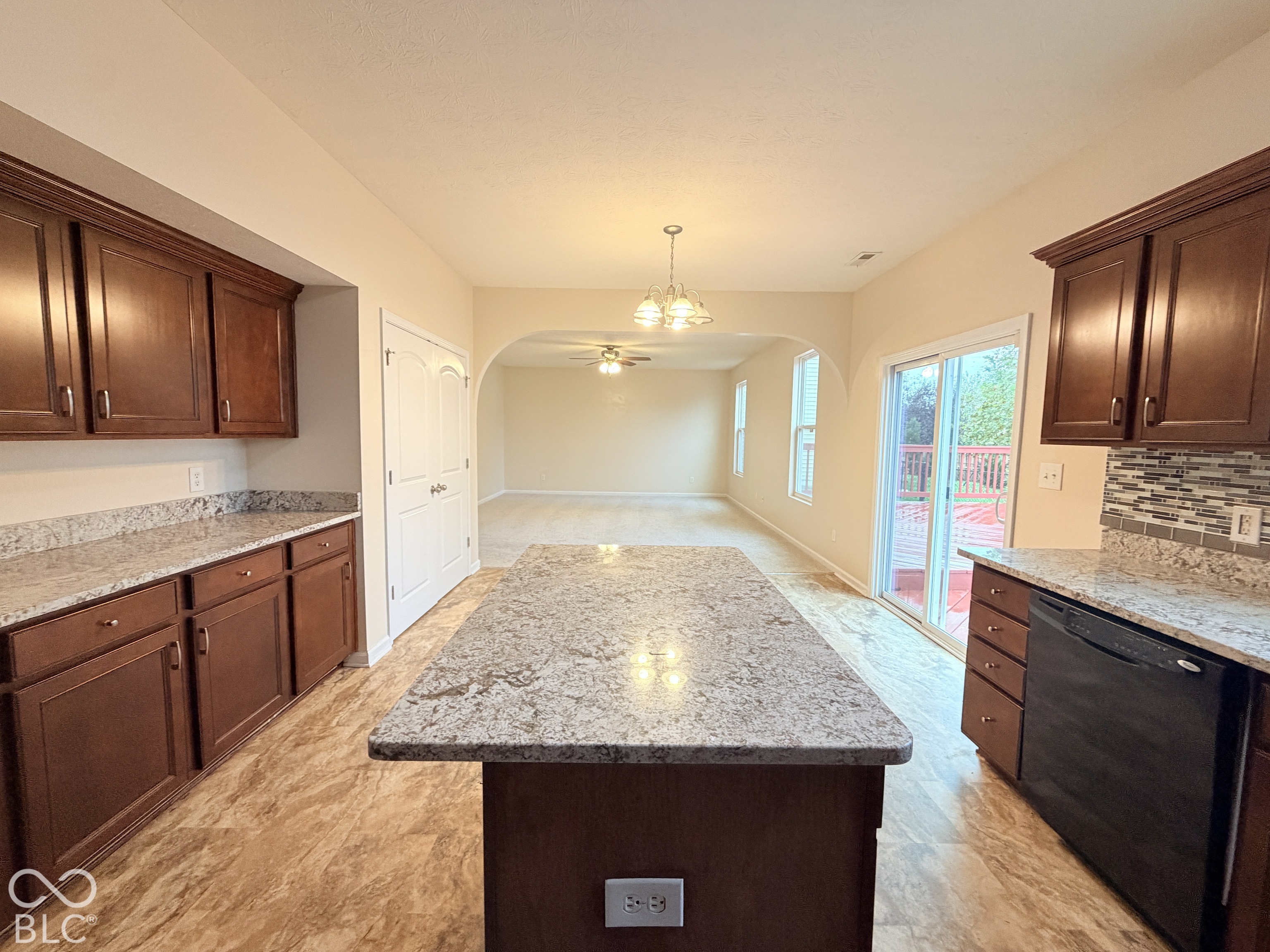 Kitchen featuring dark-finish cabinetry, stone-style countertops, a central island, a multi-colored tile backsplash, and a sliding glass door