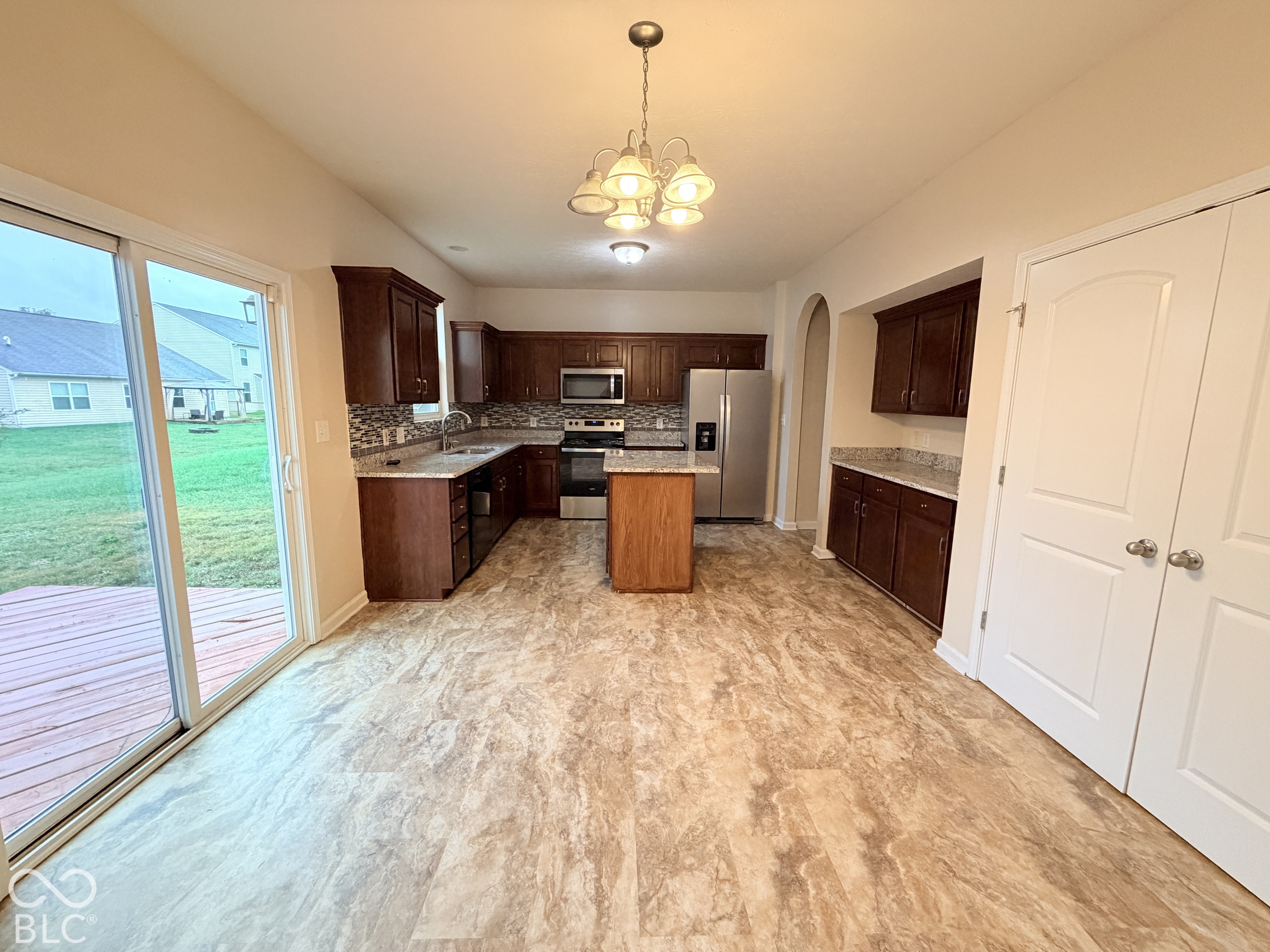 Kitchen featuring stained wood cabinetry, stone-finish countertops, a center island, stainless steel appliances, and sliding glass doors Kitchen featuring stained wood cabinetry, stone-finish countertops, a center island, stainless steel appliances, and sliding glass doors