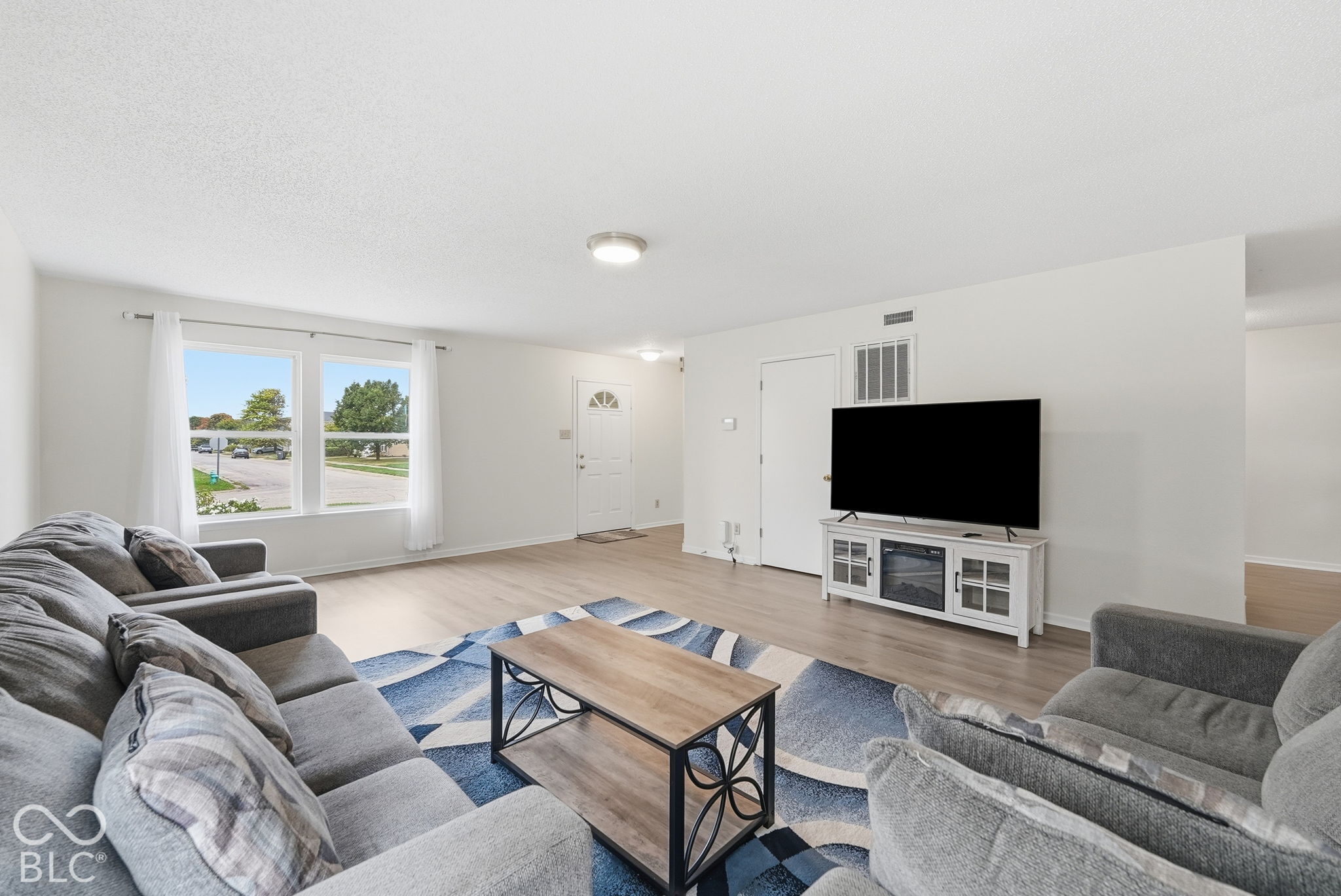 Living area featuring light-toned wood-finish flooring, neutral wall paint, and large double-pane windows Living area featuring light-toned wood-finish flooring, neutral wall paint, and large double-pane windows