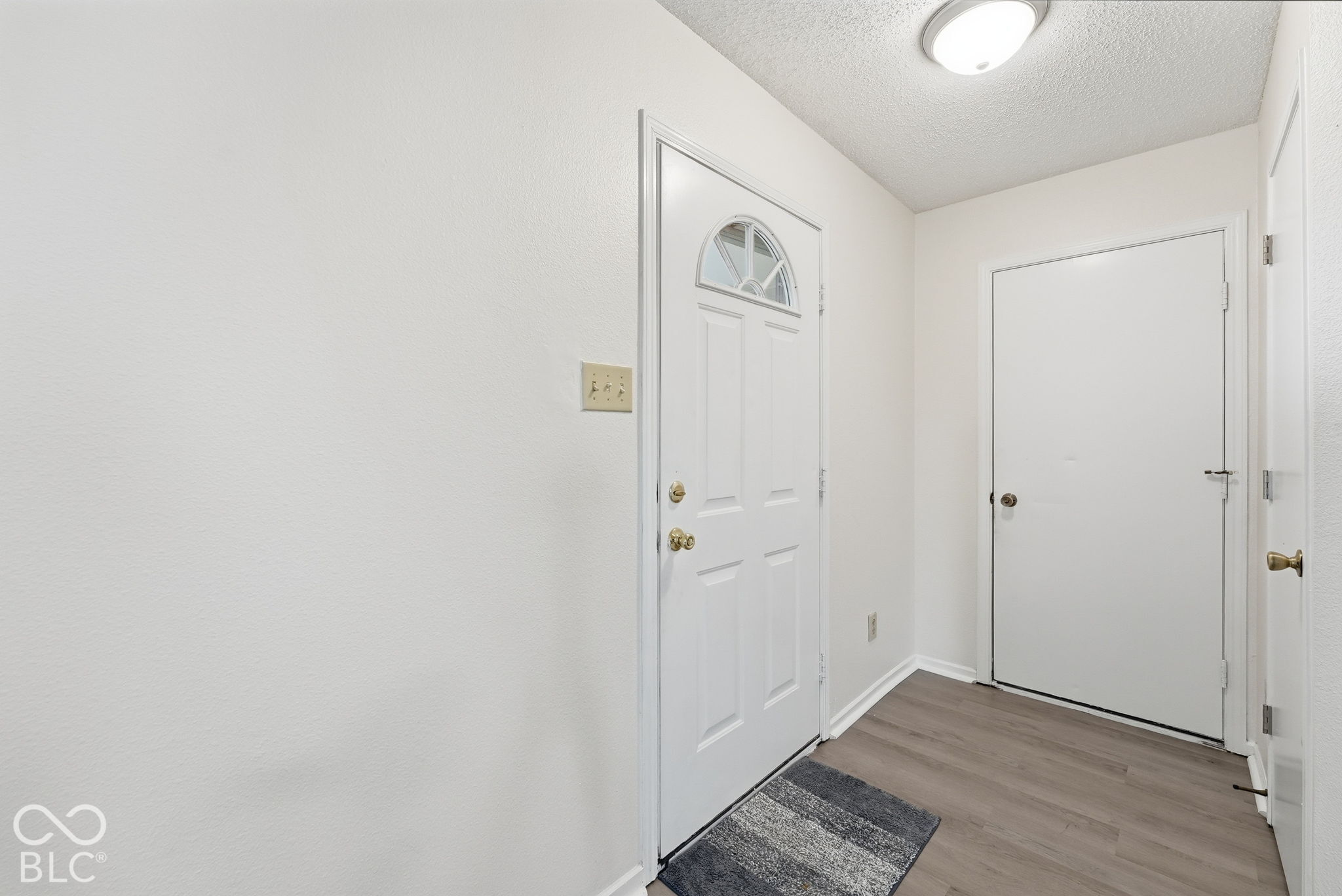 Entry featuring a white front door with a semicircular transom window, wood-finish flooring, and a flush-mount ceiling light fixture Entry featuring a white front door with a semicircular transom window, wood-finish flooring, and a flush-mount ceiling light fixture