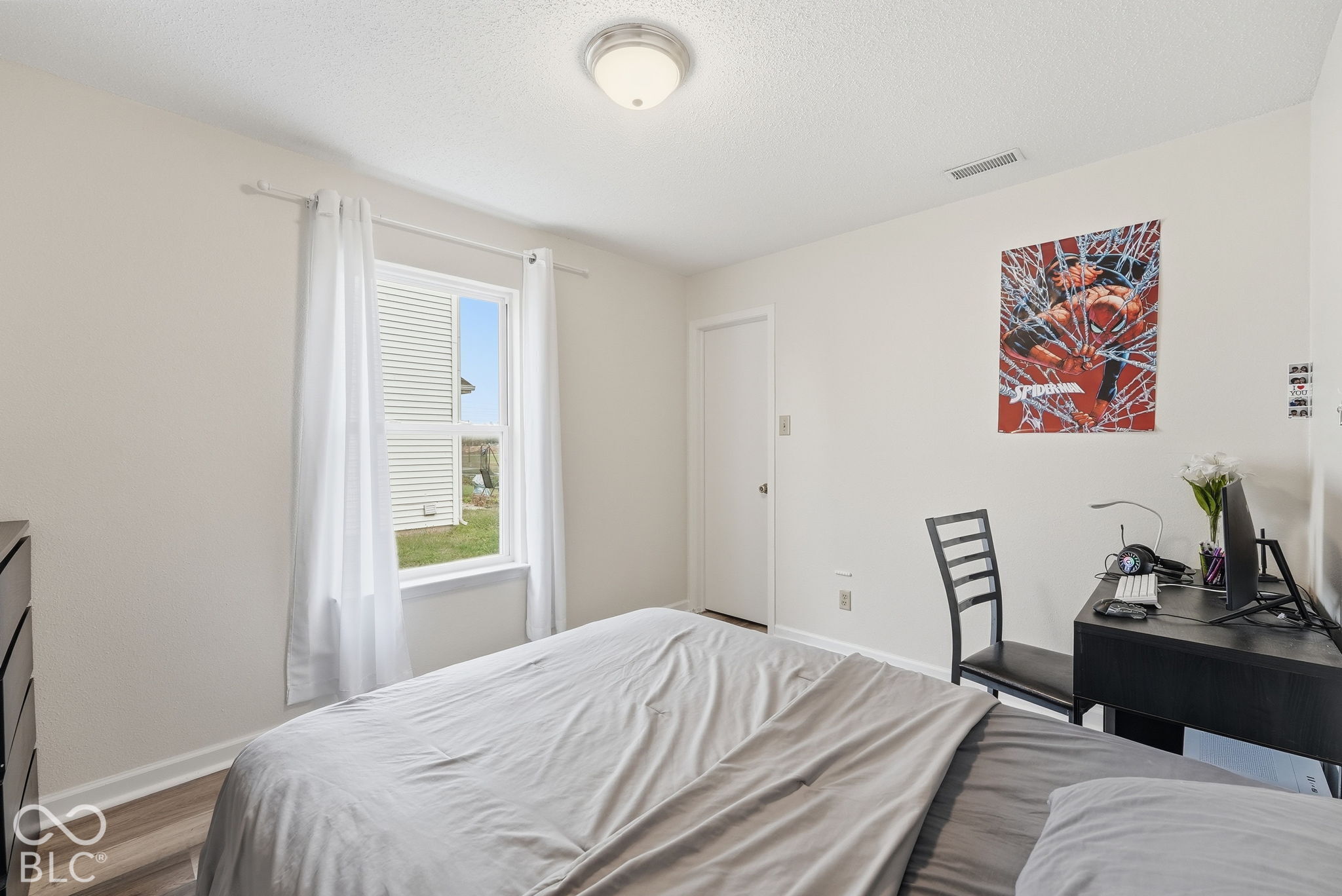 Neutral-toned room featuring wood-finish flooring, a single-hung window with a sill, a flush-mount ceiling light fixture, and a solid-core interior door