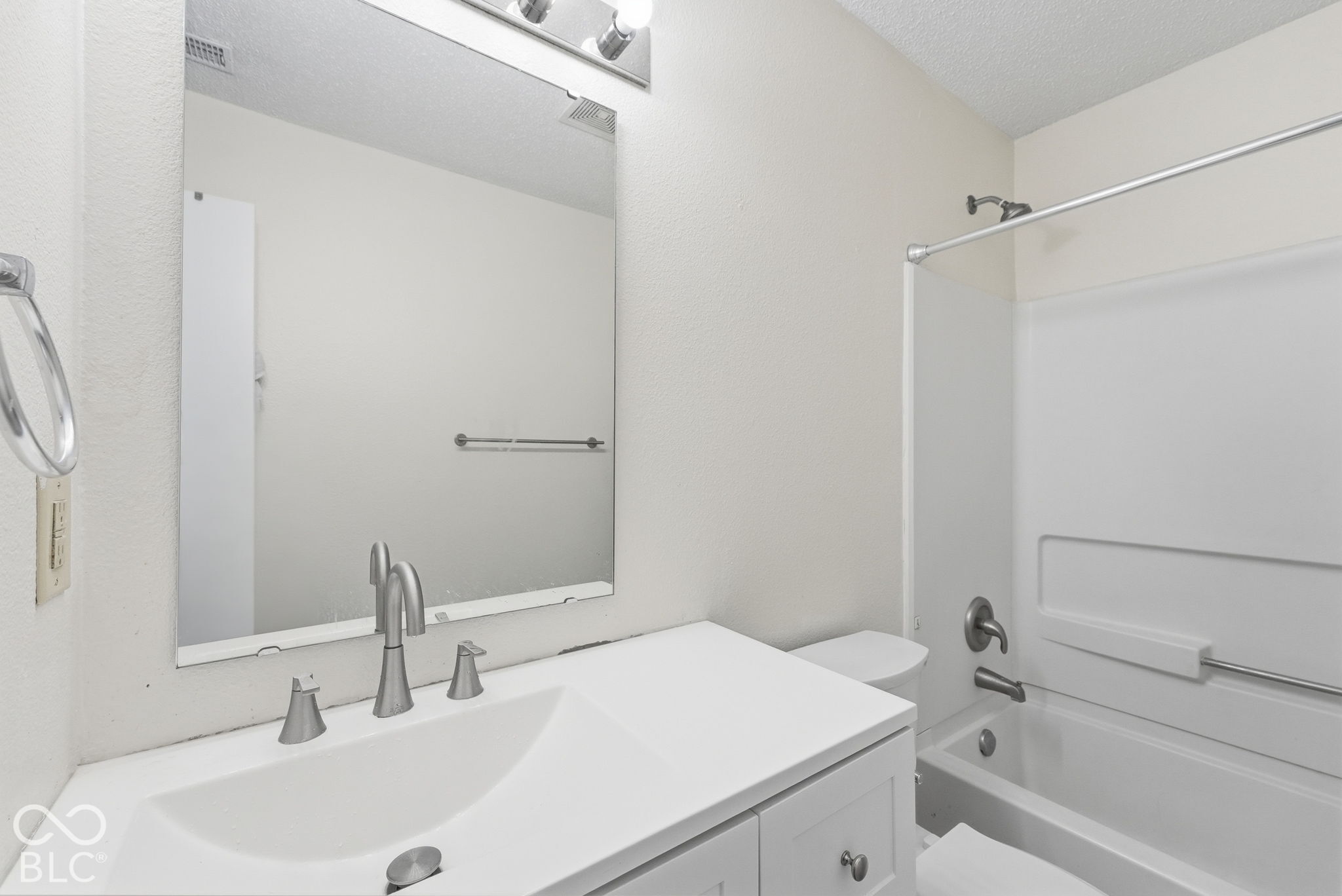 Bathroom featuring a white vanity with an integrated sink, polished metal faucet, large frameless mirror, and a combination tub and shower with a white surround