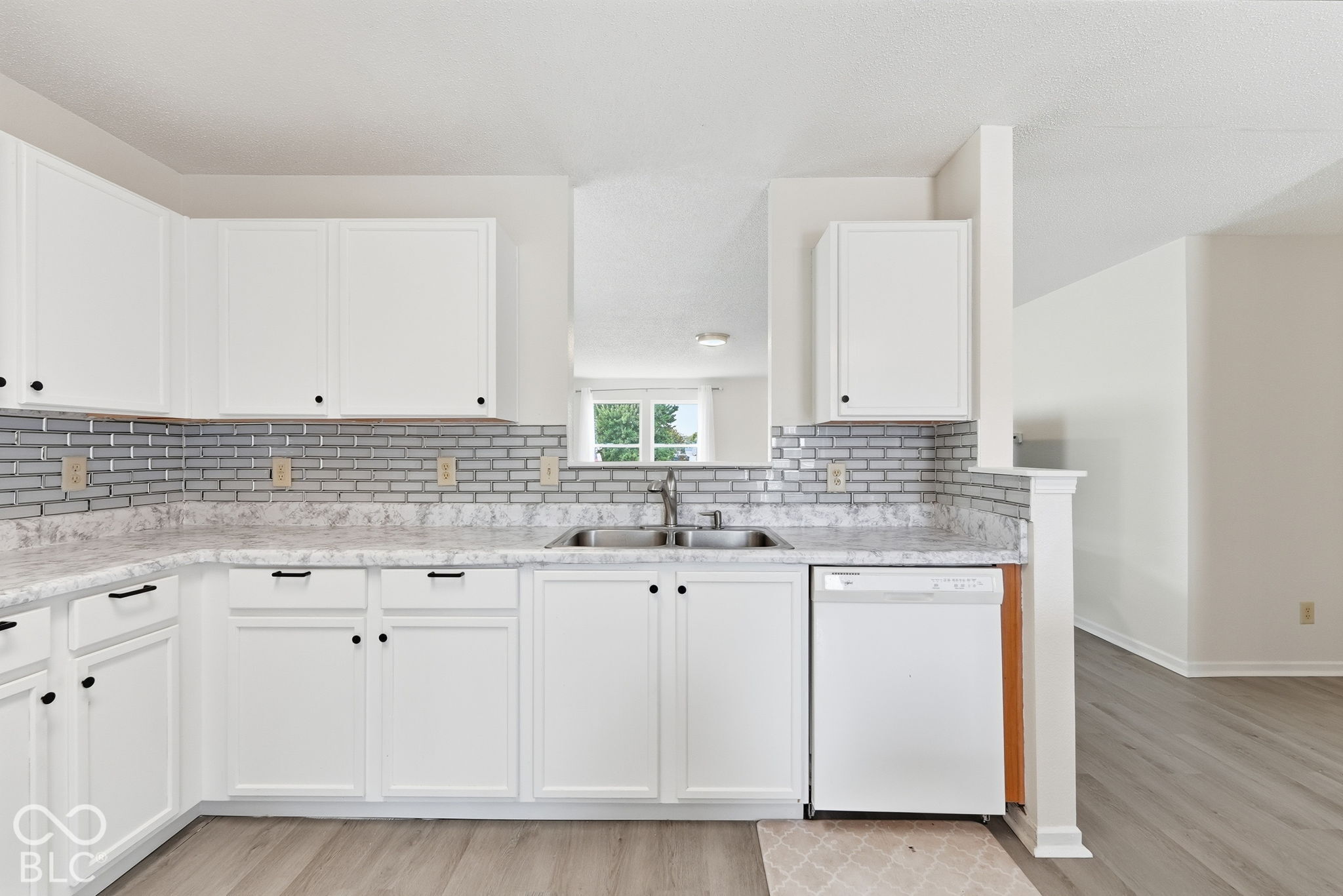 Kitchen featuring white cabinetry, stone-patterned countertops, a subway tile backsplash, a dual-basin stainless steel sink with a pull-down faucet, and a built-in dishwasher