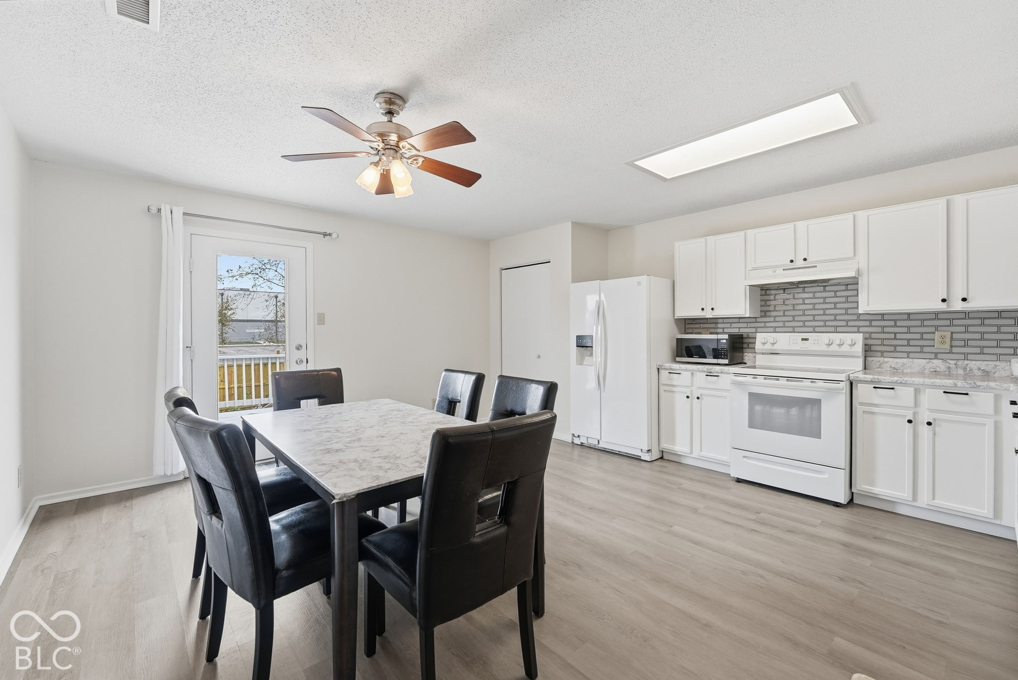 Kitchen featuring white cabinetry, stone-finish countertops, a grey subway-style tile backsplash, wood-finish flooring, and a ceiling fan with integrated lighting