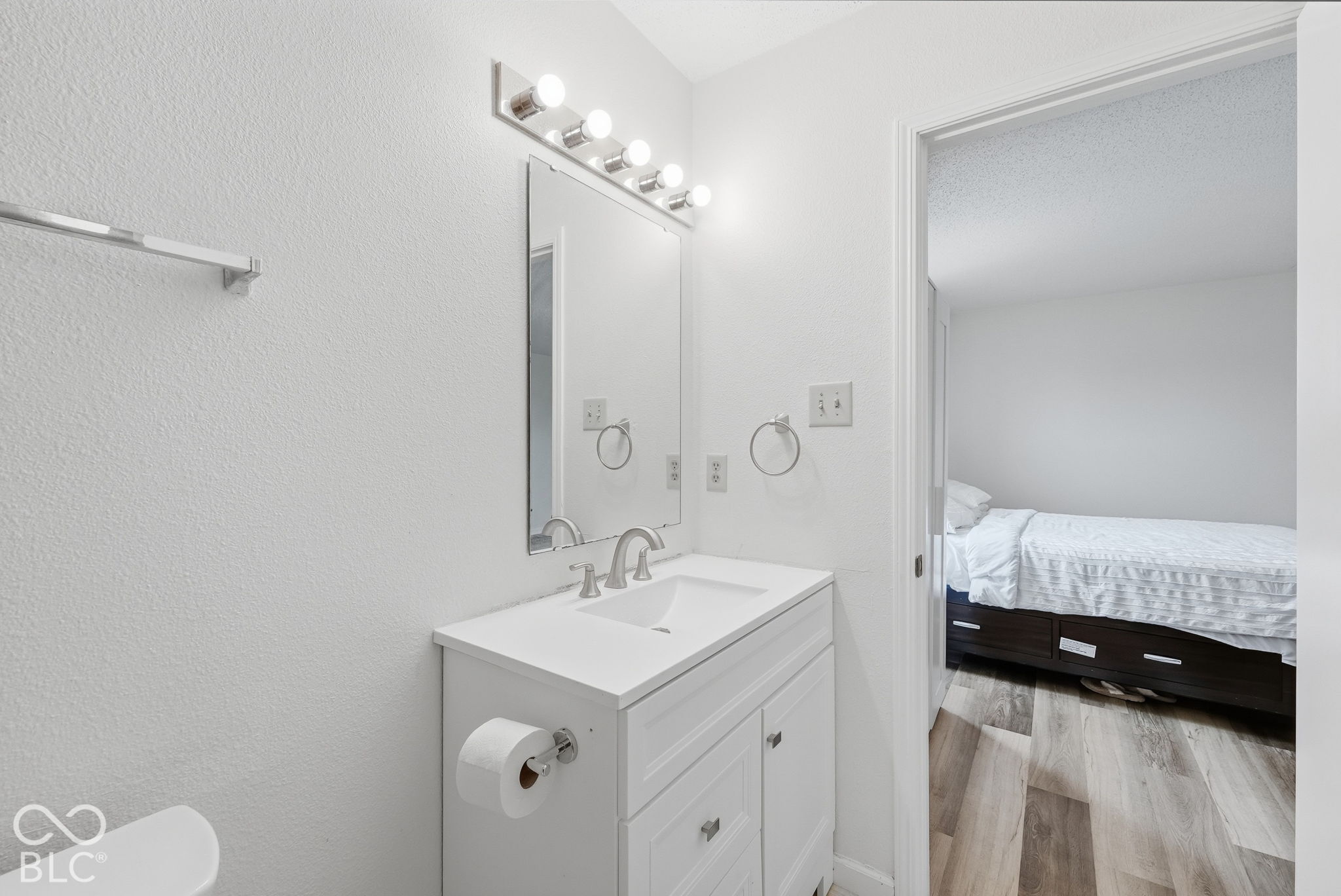 Bathroom featuring a white vanity cabinet with an integrated sink, polished metal faucet, rectangular wall mirror, and five-bulb vanity light fixture