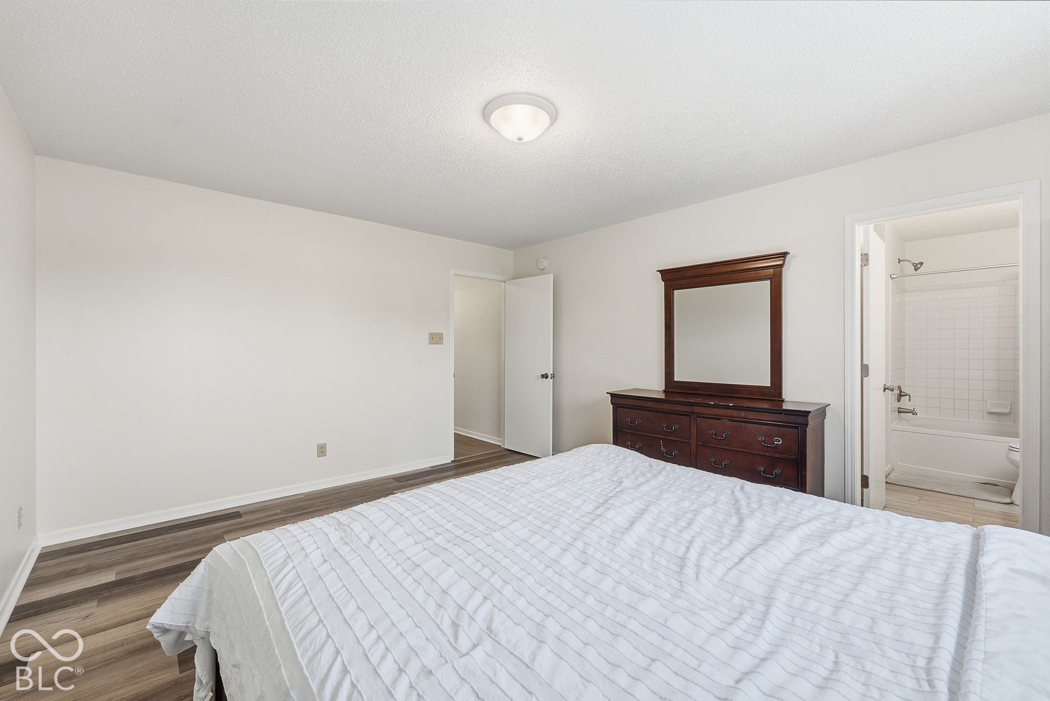 Room featuring wood-finish flooring, a flush-mount ceiling light, and interior doorway access to a bathroom with a tiled tub surround