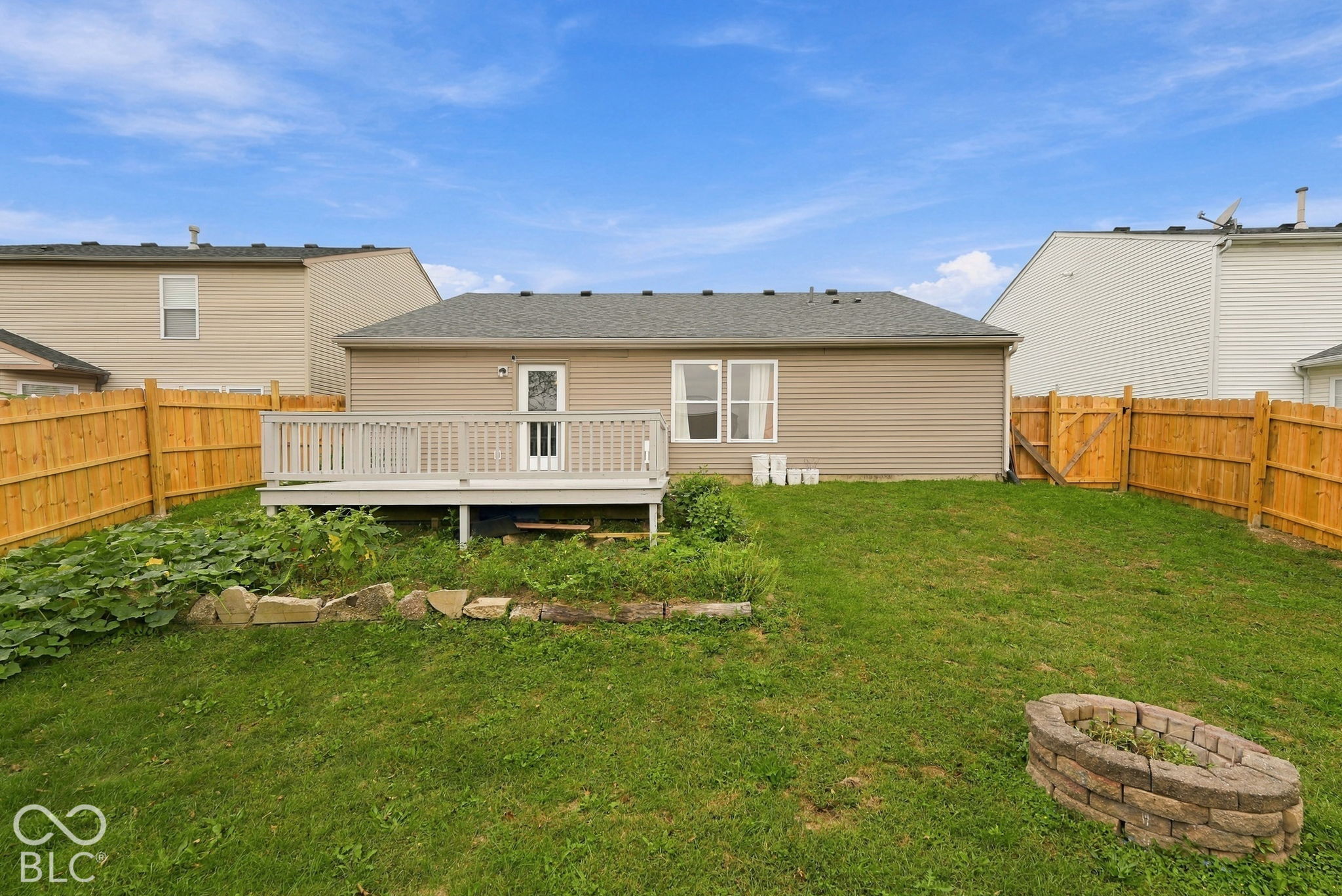 Rear exterior featuring vinyl siding, an elevated wood deck, and a fenced backyard with a stone-accented fire pit