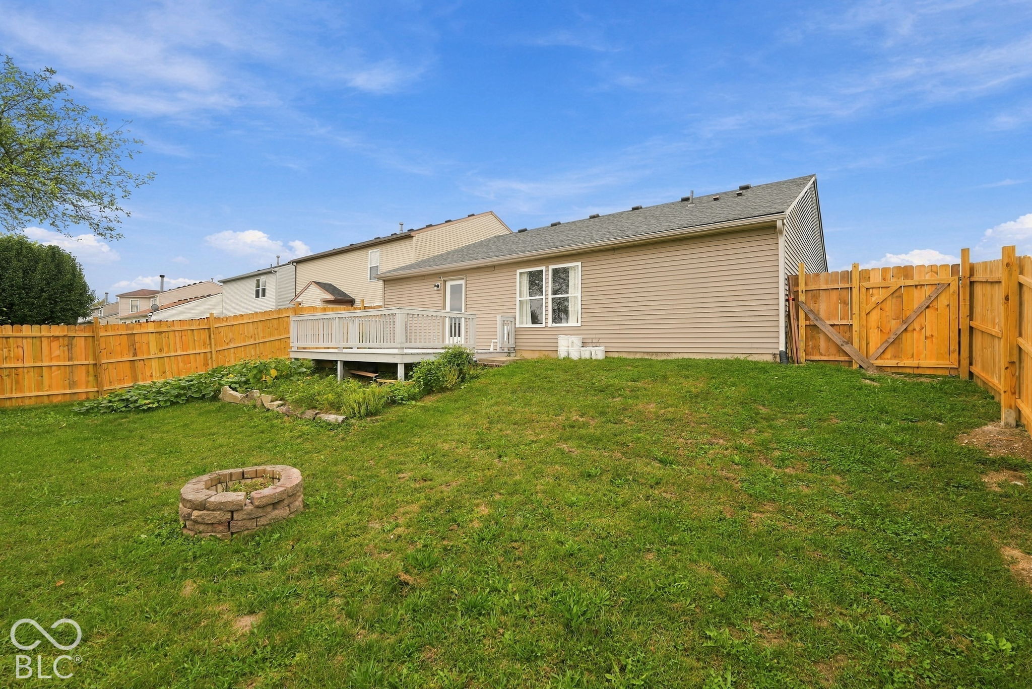 Rear exterior featuring vinyl siding, an elevated wood deck, a fenced backyard, and a stone-style fire pit