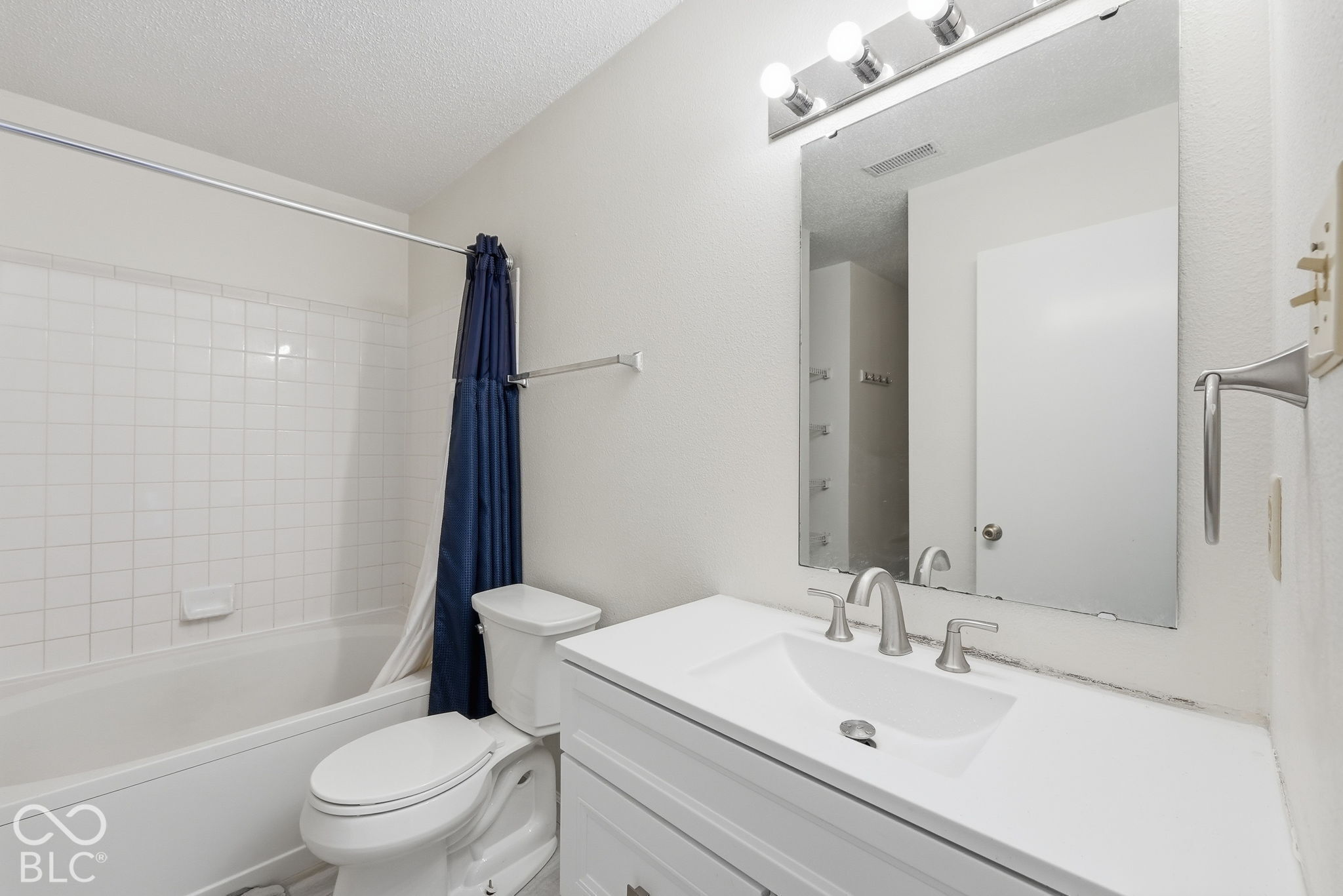Bathroom featuring a white vanity with an integrated sink, brushed-nickel widespread faucet, large wall-mounted mirror, four-light vanity fixture, and a tiled shower-tub combination