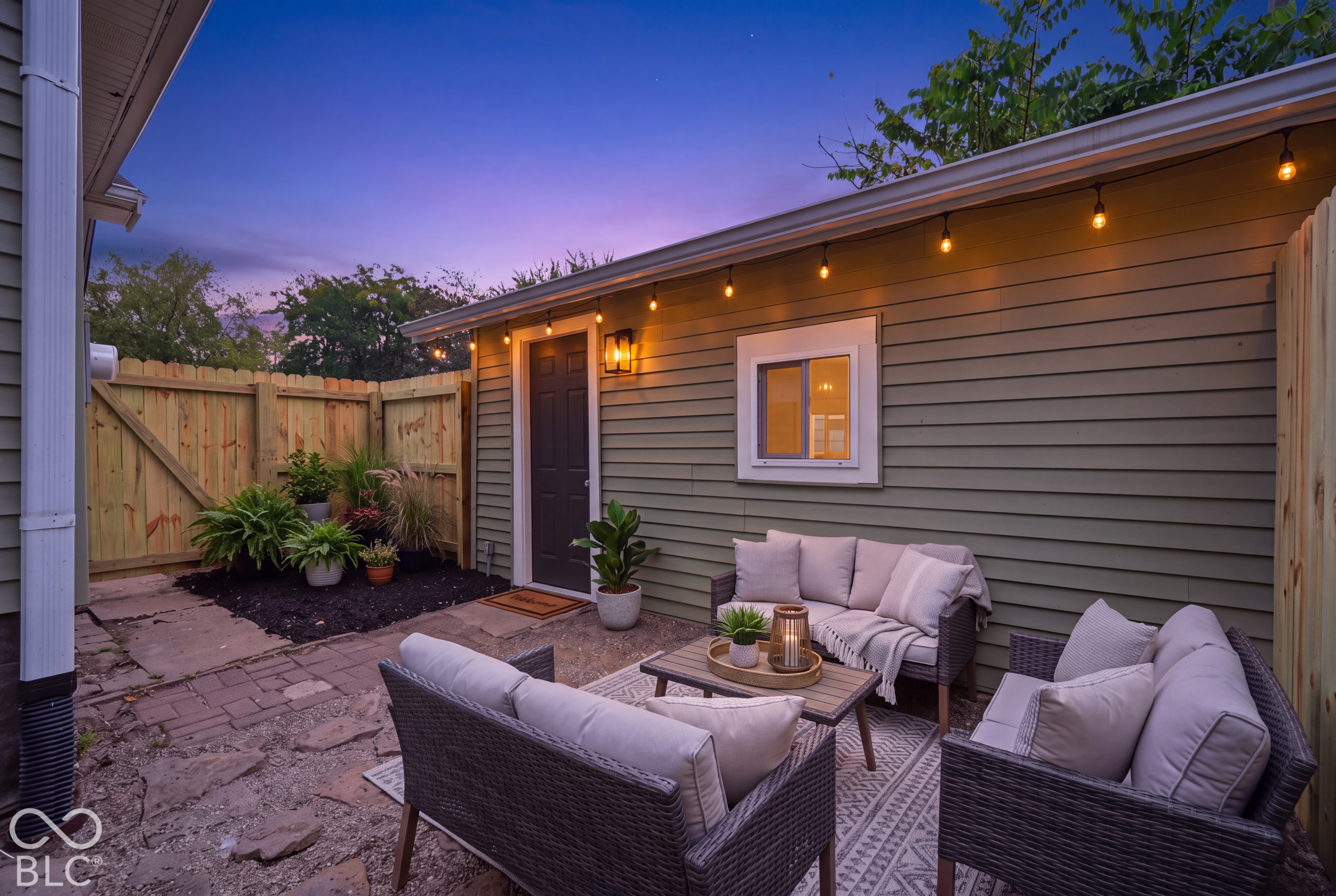 Private courtyard featuring horizontal siding, flagstone hardscaping, a raised wood fence, and mounted string lighting