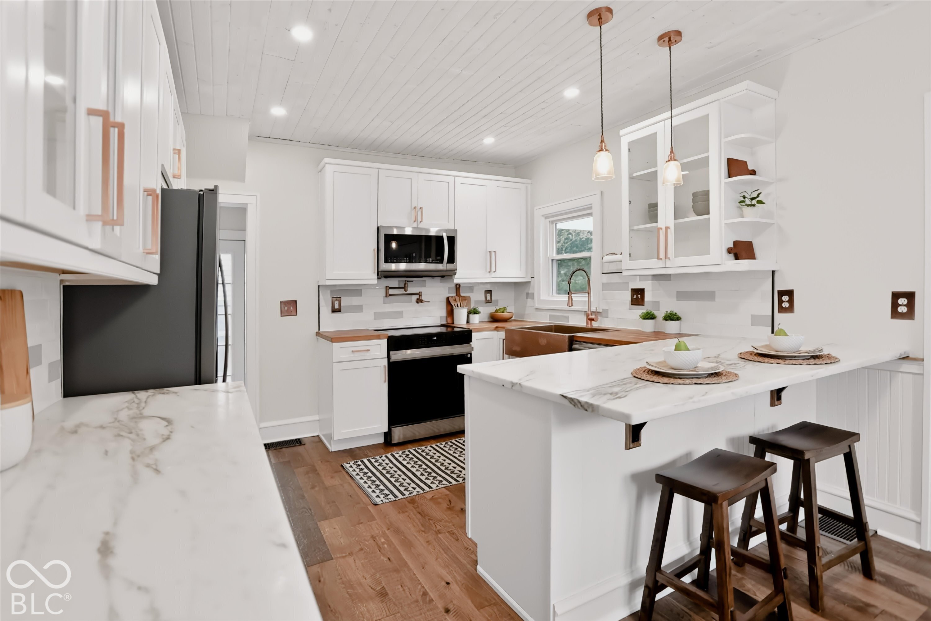 Kitchen featuring white shaker-style cabinetry with copper-toned hardware, stone-finish countertops, wood-finish flooring, a farmhouse sink with a wall-mounted faucet, and a tongue-and-groove ceiling