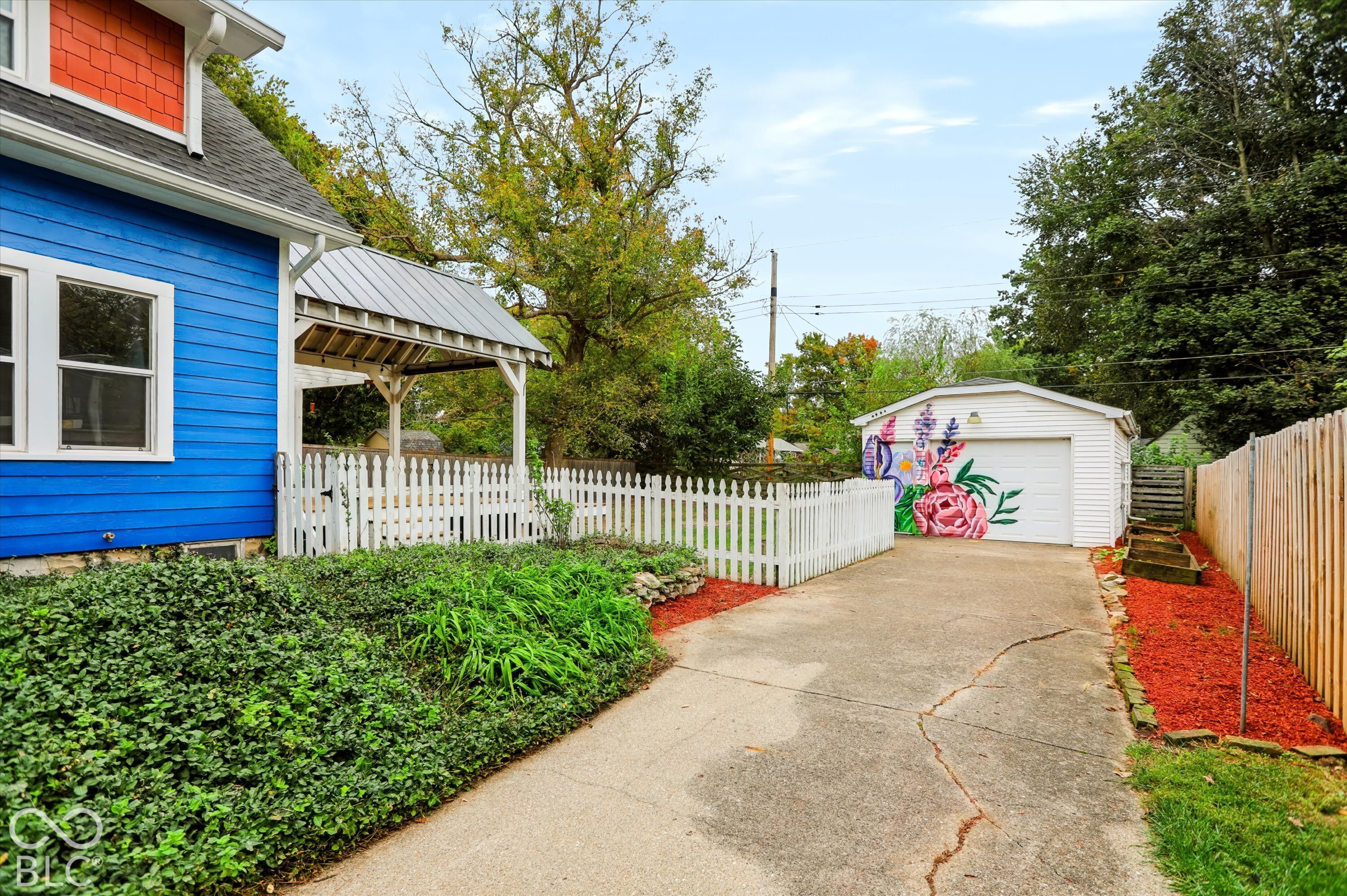 Exterior featuring horizontal lap siding, a metal-roofed covered porch, white picket fencing, a detached garage, and a concrete driveway