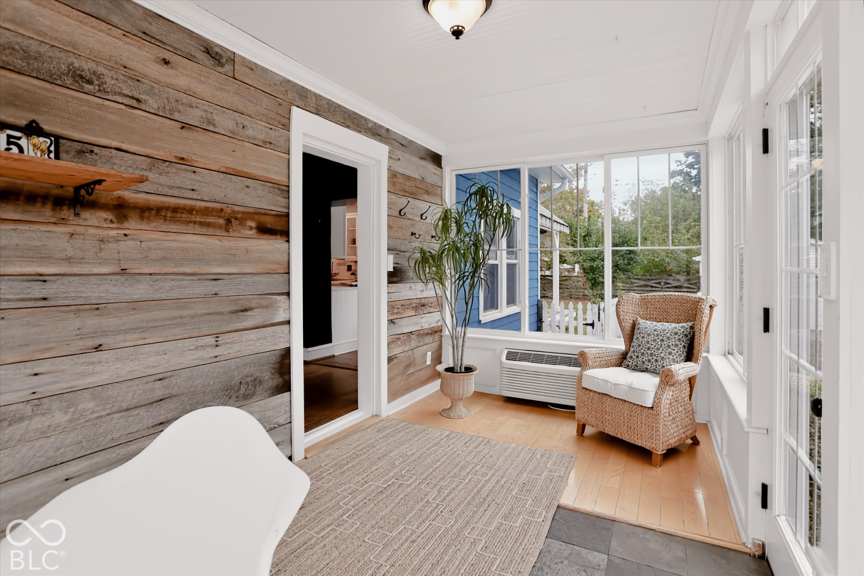 Enclosed sunroom featuring rustic horizontal wood-plank walls, expansive multi-pane windows, wood-finish flooring, and a tiled threshold
