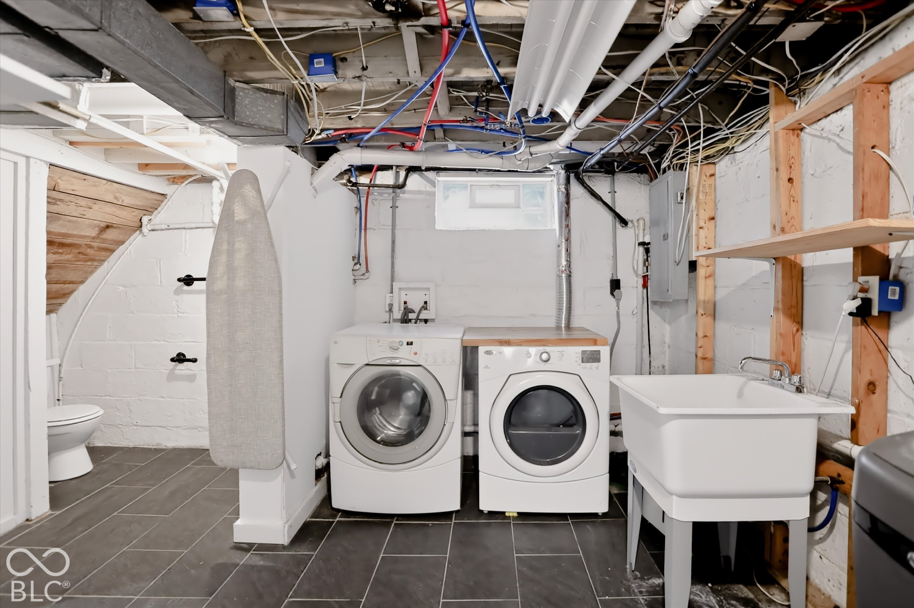 Utility area featuring dark floor tiling, integrated washer and dryer, deep basin utility sink, and built-in wood shelving