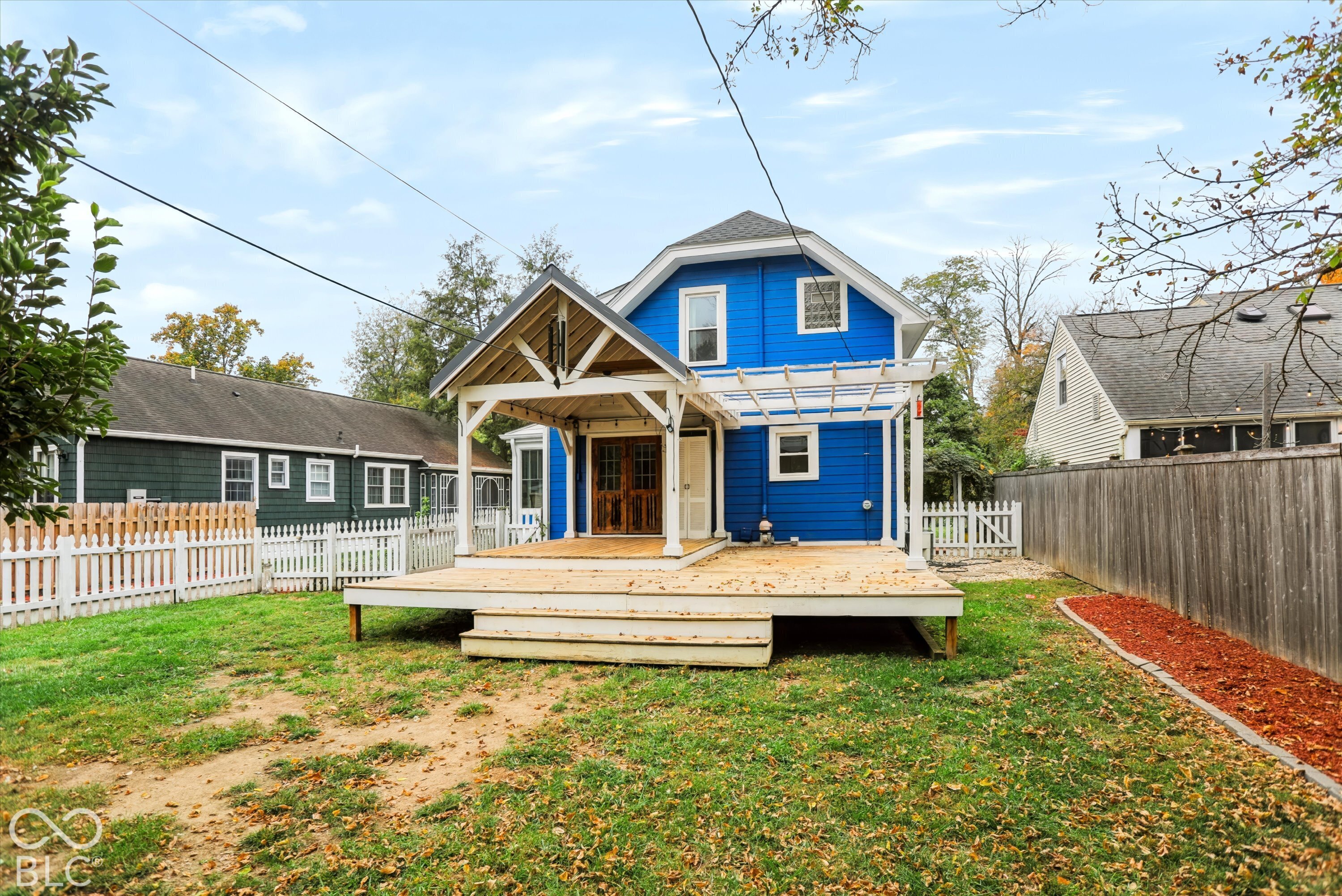 Rear exterior featuring a spacious wood deck, timber-framed covered porch, attached white pergola, and perimeter wood fencing