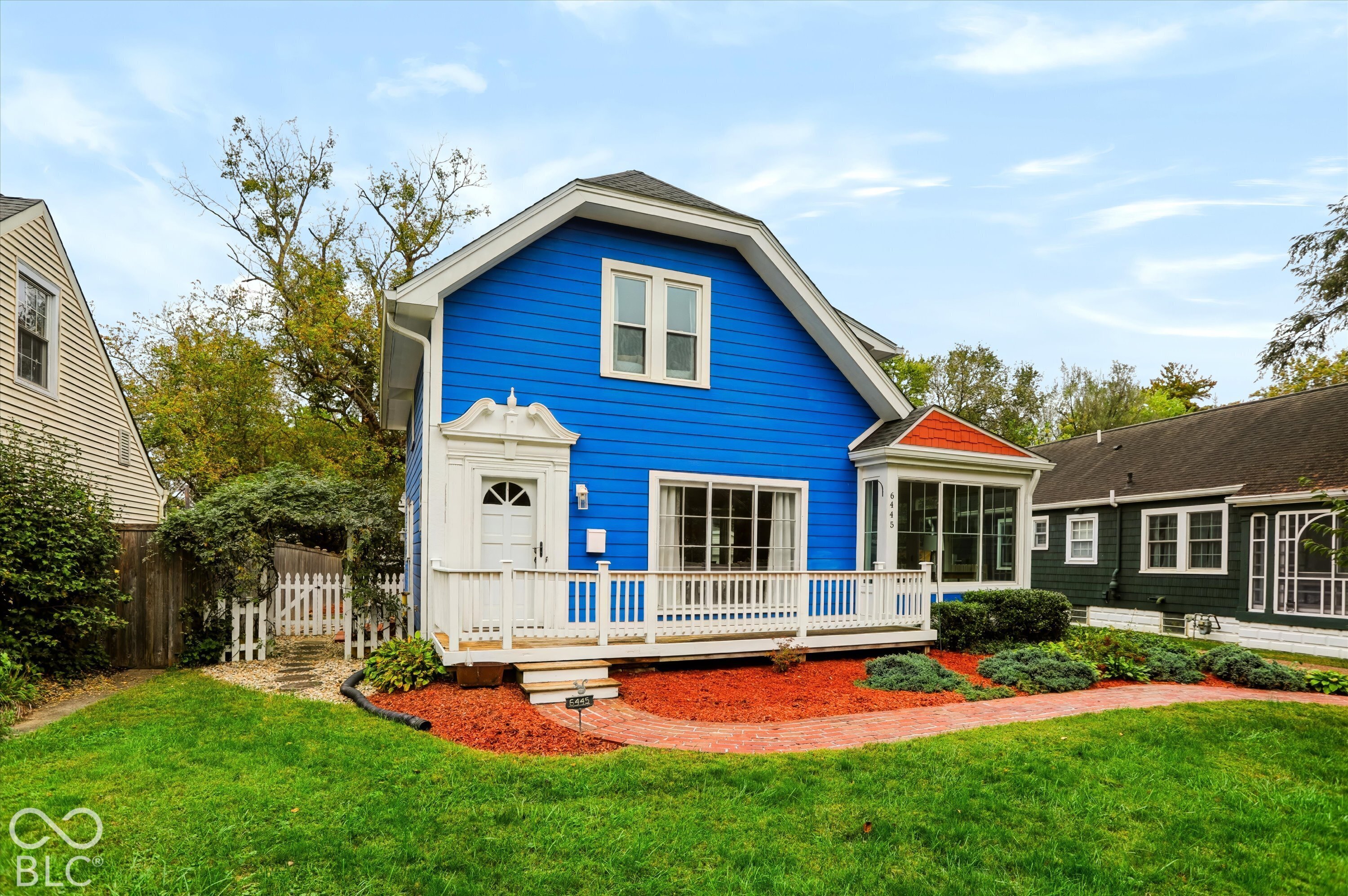 Two-story residence featuring lap siding, an expansive front deck with white railings, a front-facing sunroom with multi-pane windows, decorative door trim, and a brick-paved walkway