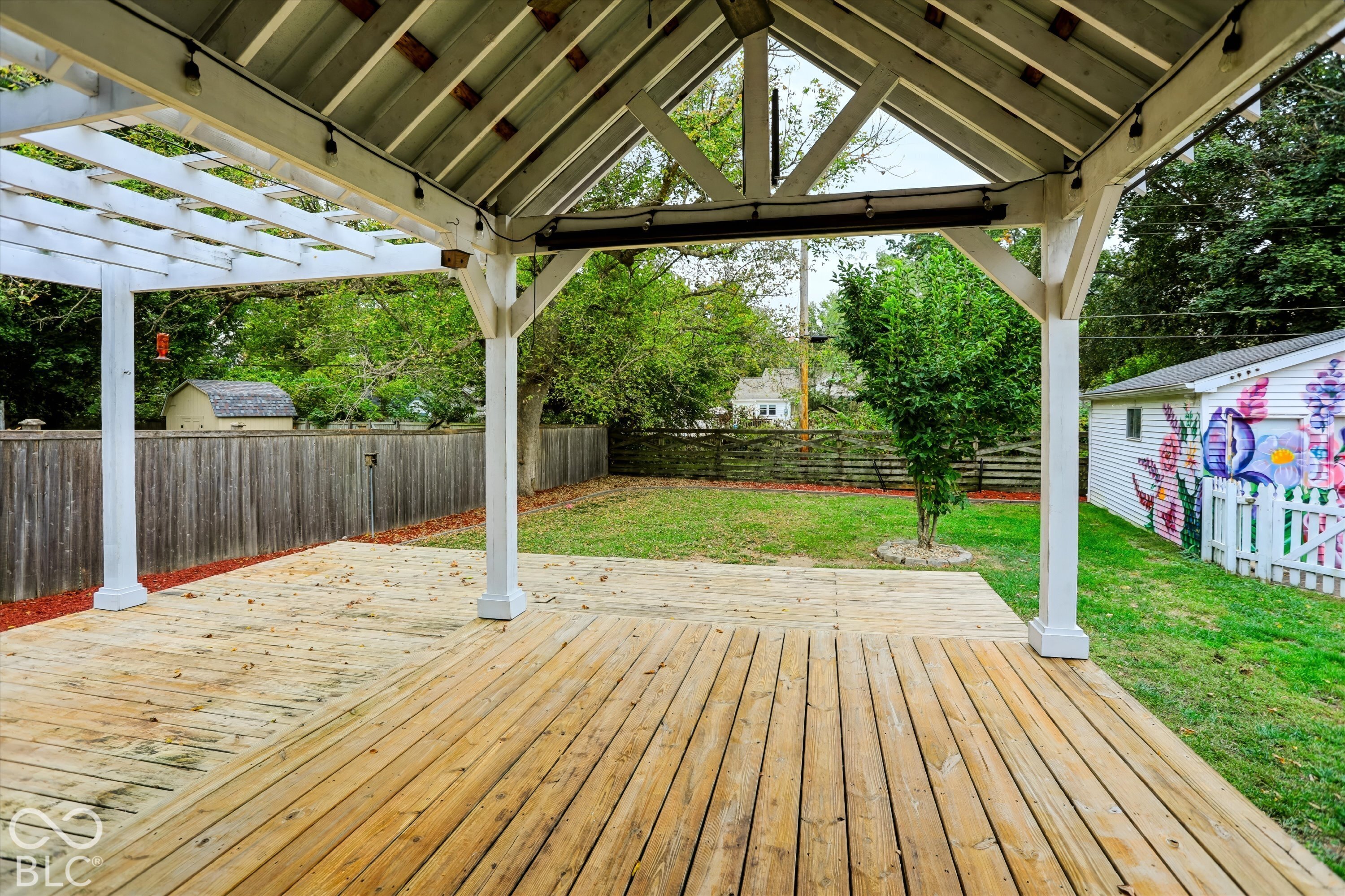 Covered wooden patio featuring a vaulted timber-frame structure, a wooden pergola extension, and a fenced backyard