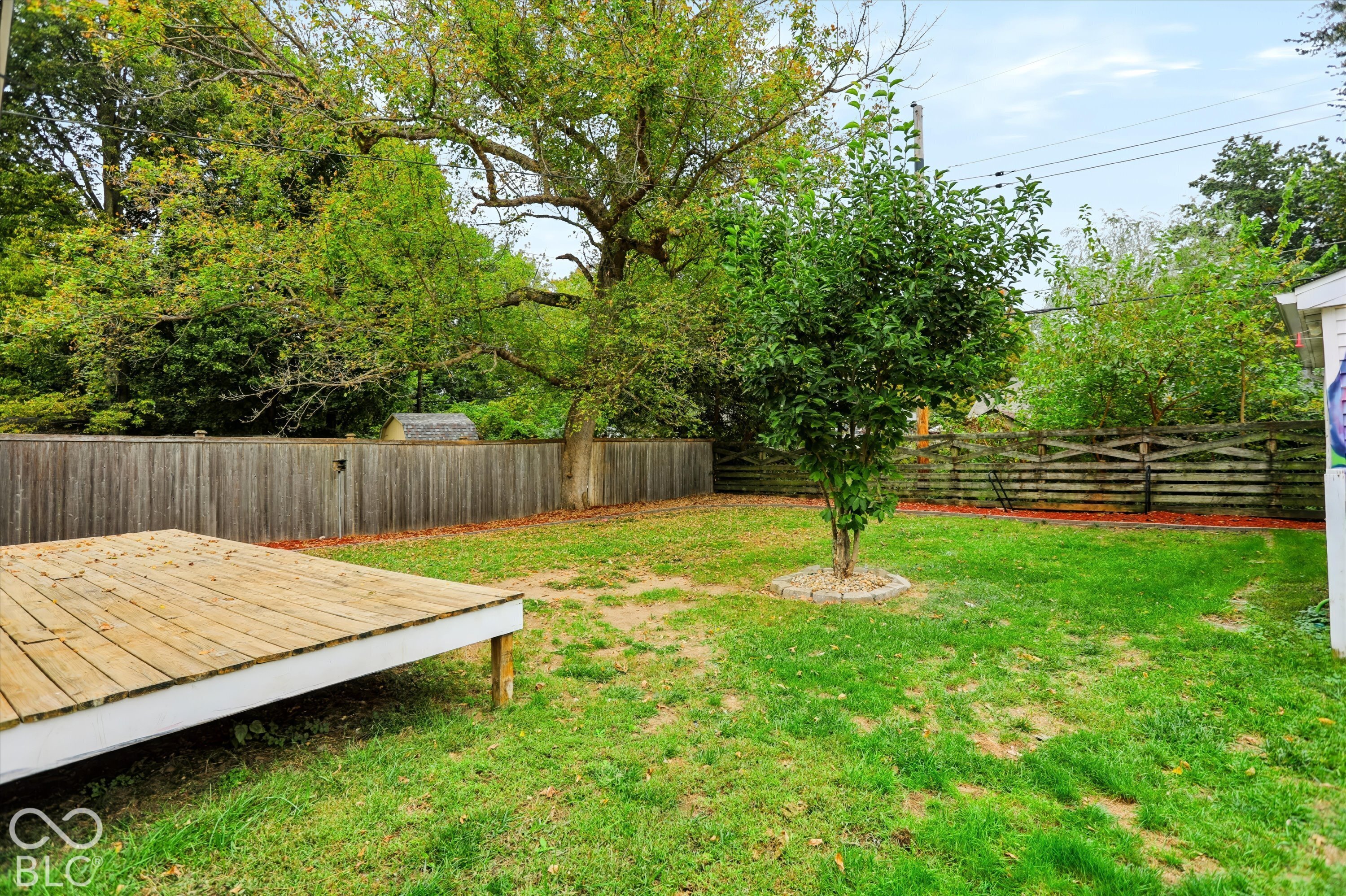 Backyard featuring a wood-plank deck, perimeter wood fencing, and mature trees