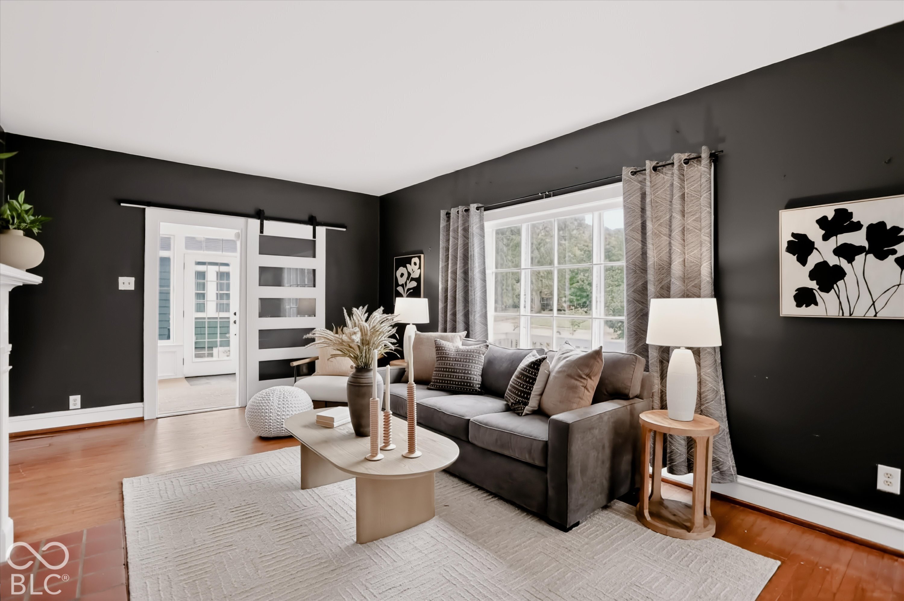 Living space featuring wood-finish flooring, a white sliding barn-style door with glass panels, a large multi-pane window, and a fireplace mantel
