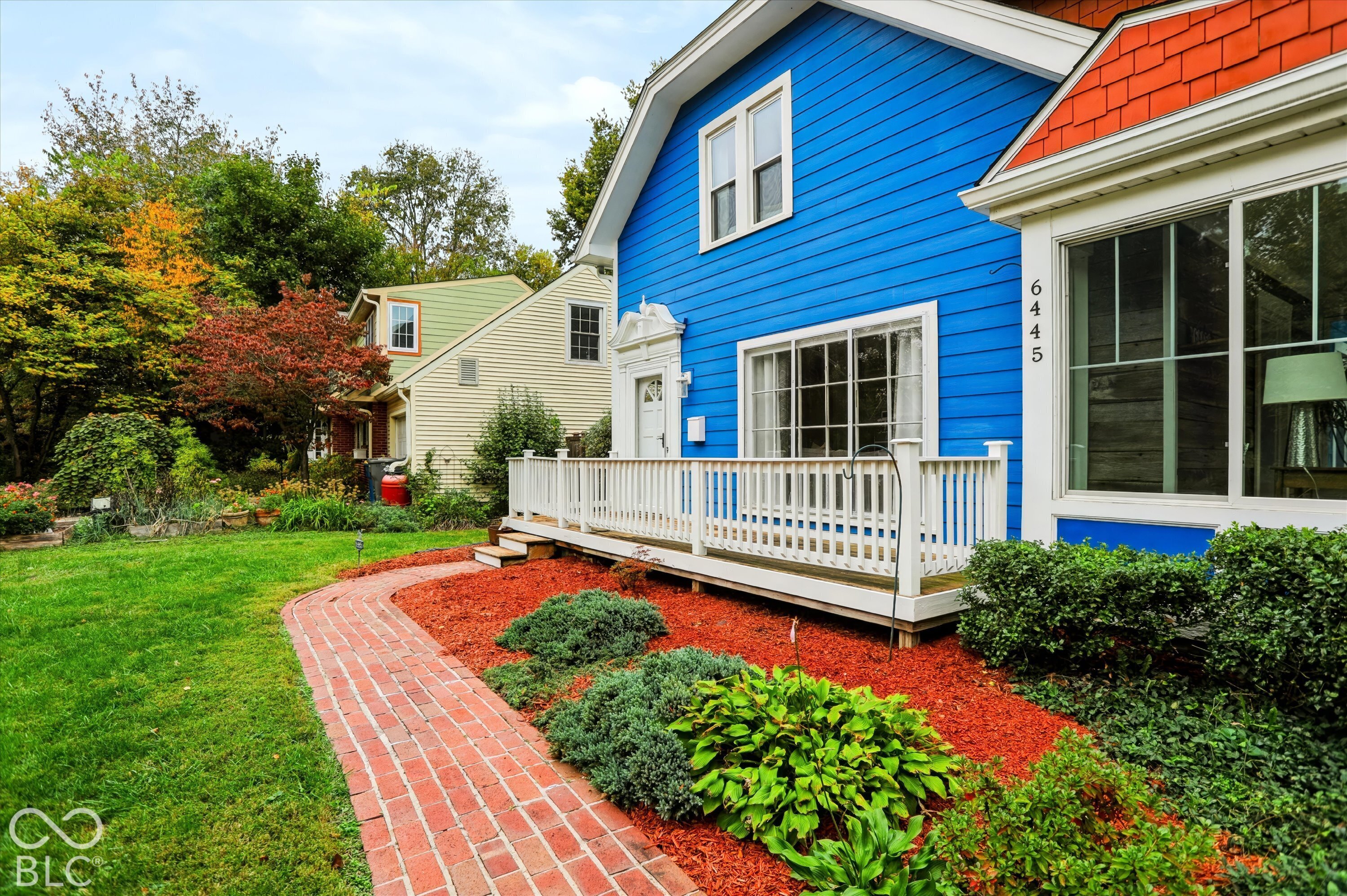 Exterior featuring lap siding, shake shingle accents, a white railing porch, and a brick walkway surrounded by landscaped gardens