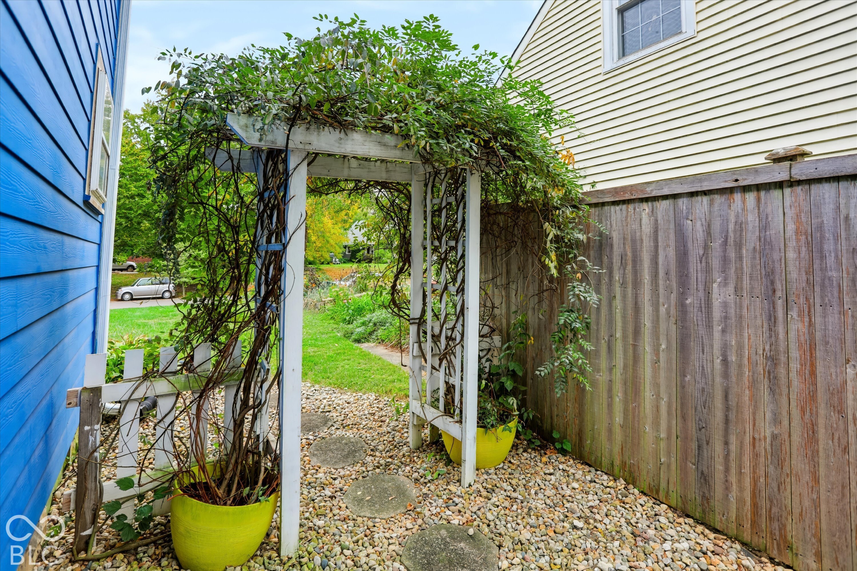 Outdoor space featuring a white garden arbor, pea gravel ground cover, stepping stones, and a wood privacy fence
