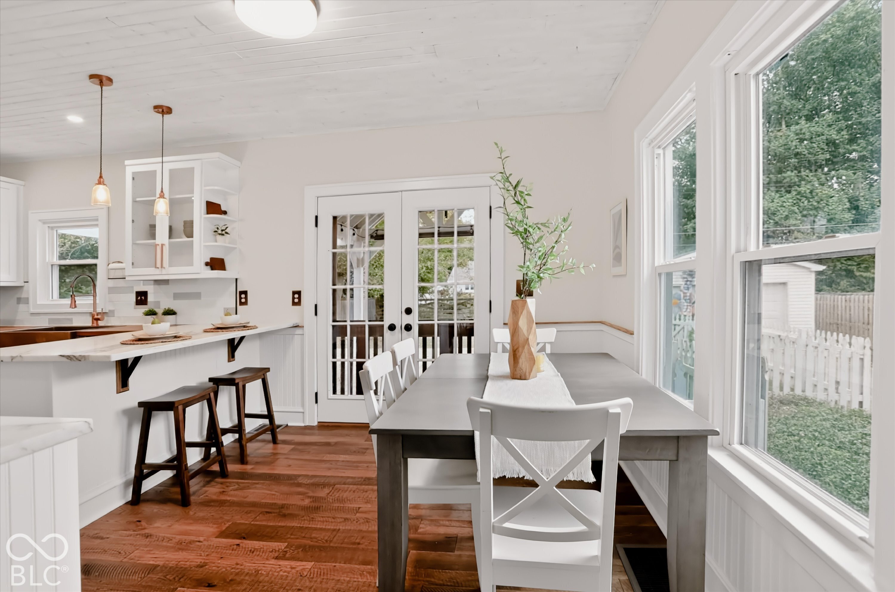 Kitchen featuring wood-finish flooring, white built-in cabinetry with glass-front uppers, a peninsula with stone-finish countertop, dual pendant lighting, and multi-lite French doors