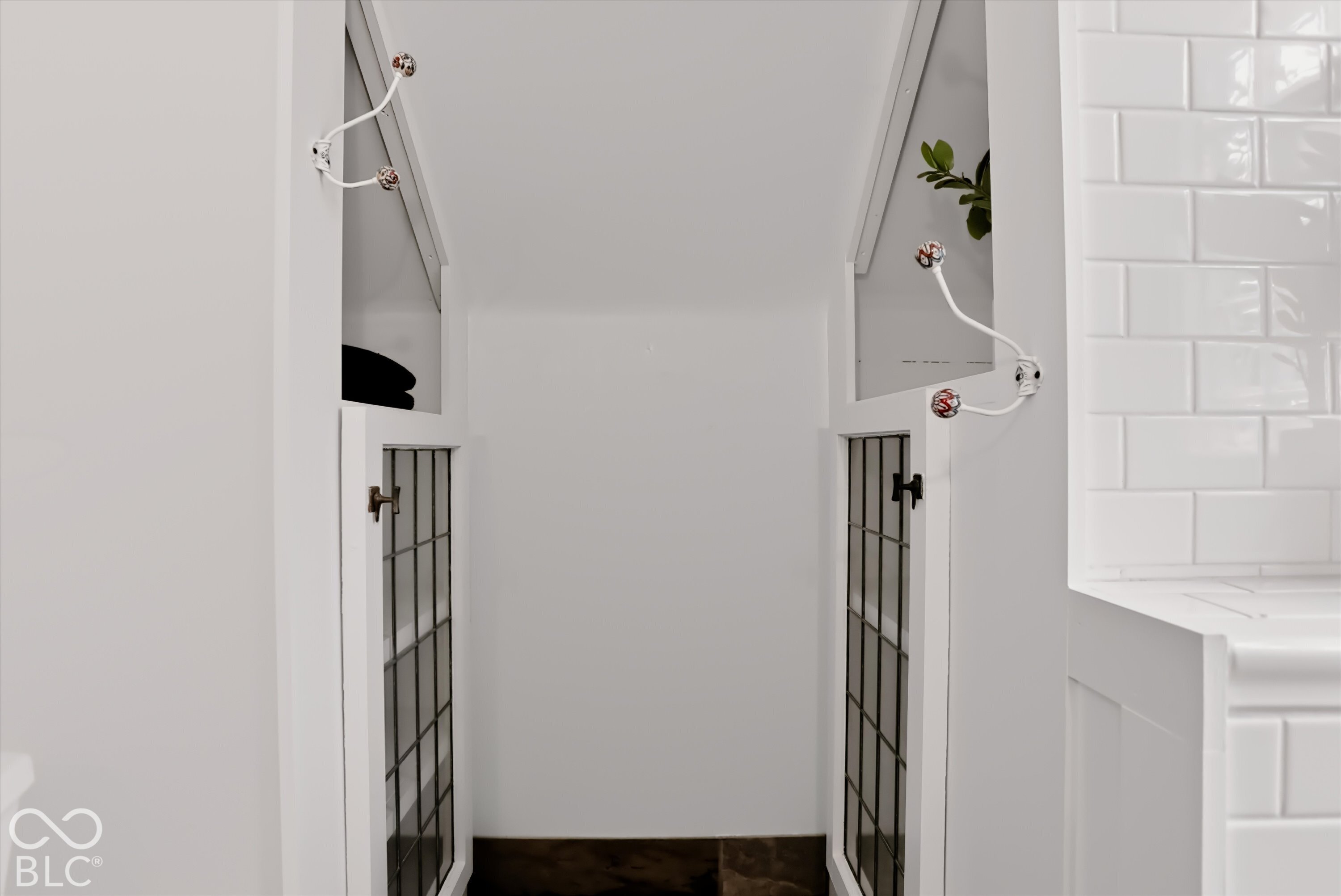 Built-in cabinetry featuring white frames, glass-paneled doors, and ornamental wall-mounted hooks, complemented by white subway tile wall cladding