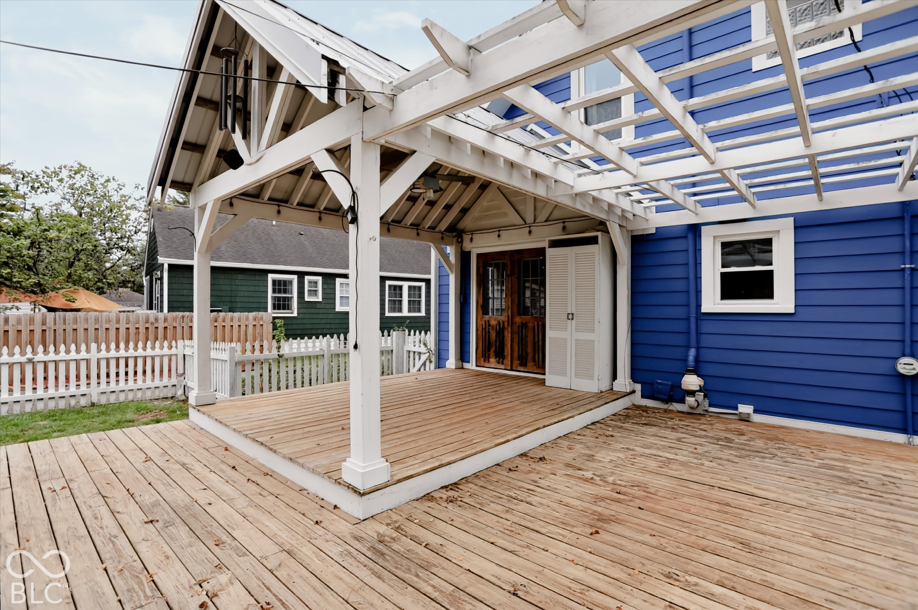 Spacious wood deck featuring a covered pergola, white lap siding, and double wooden exterior doors