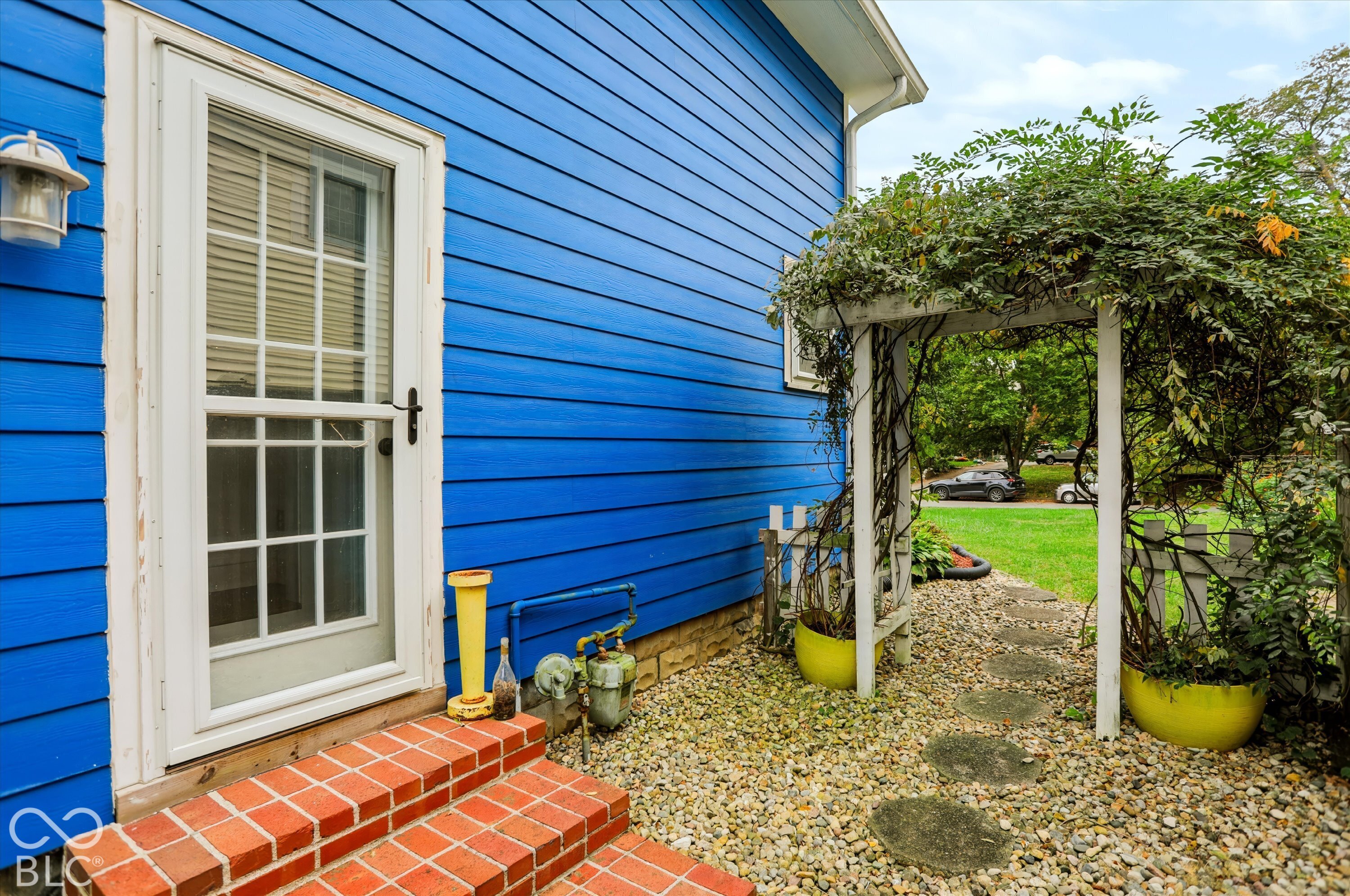 Exterior featuring horizontal lap siding, a red brick step entry with a glass-paneled storm door, and a wooden garden arbor over a stone paver path