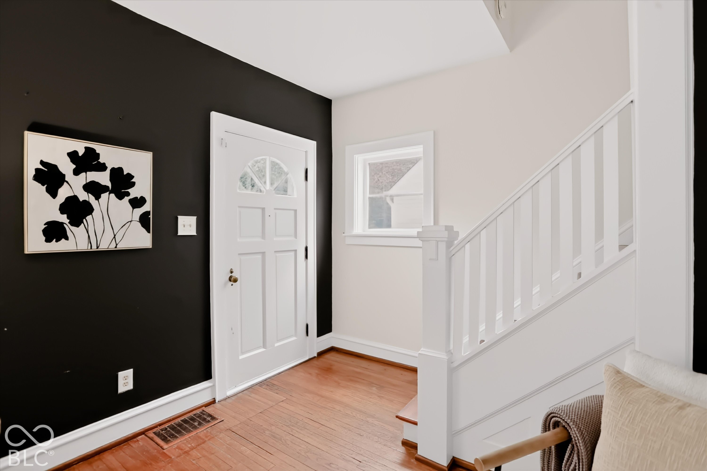 Entryway featuring hardwood flooring, a white-painted wooden staircase with a square-profile newel post, a six-panel exterior door with a decorative transom window, and high-contrast dual-tone wall paint