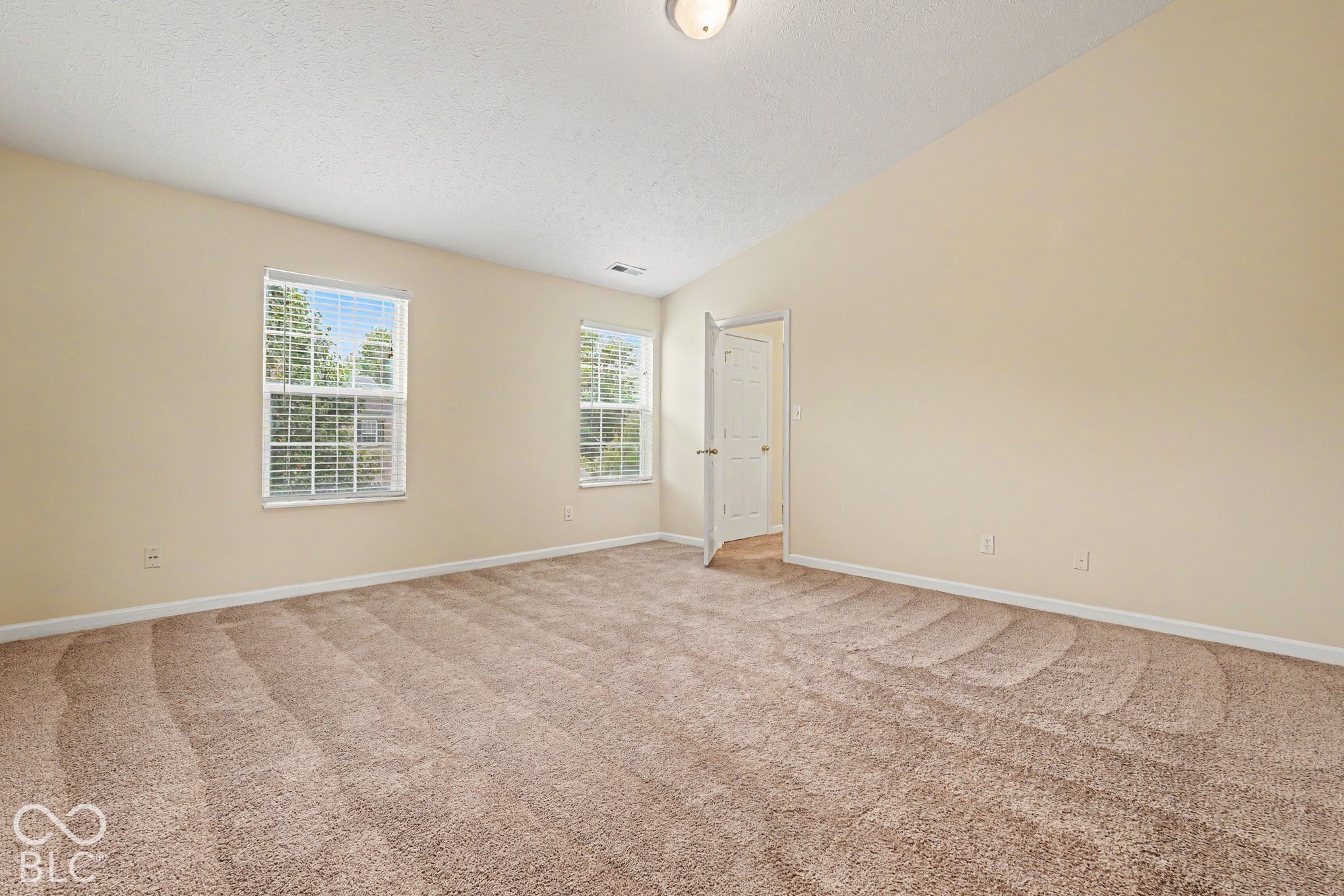 Room featuring vaulted ceilings, neutral wall tones, wall-to-wall carpeting, and multiple windows