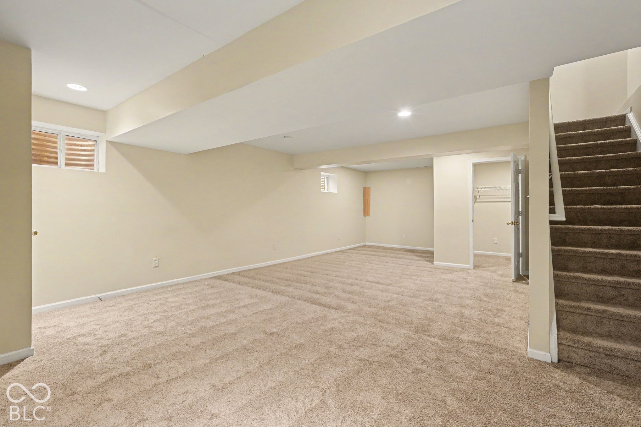 Open-concept room featuring neutral wall-to-wall carpeting, recessed lighting, egress windows, and built-in closet storage