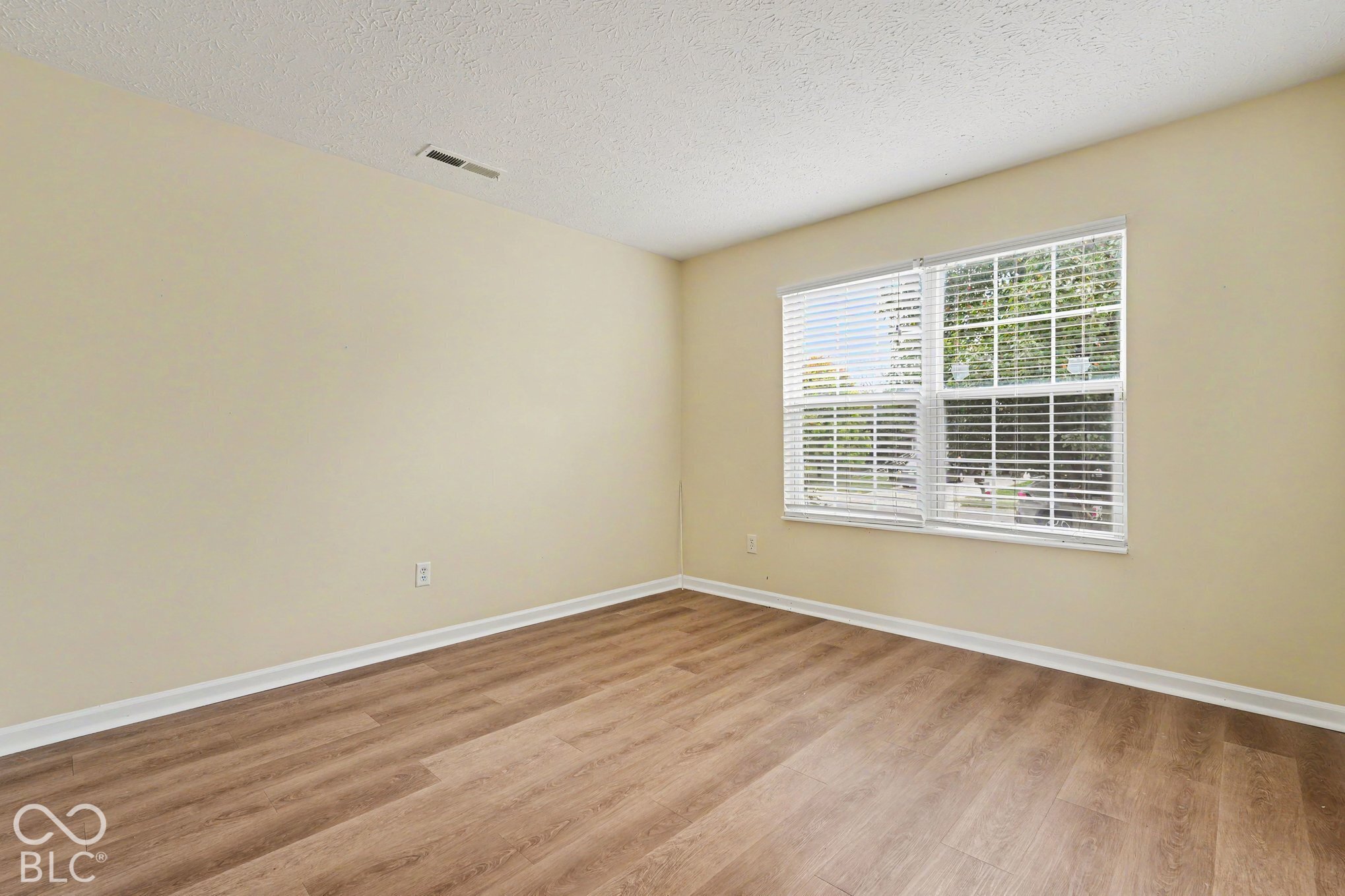 Neutral-toned walls, wood-finish flooring, and a multi-pane window with adjustable blinds